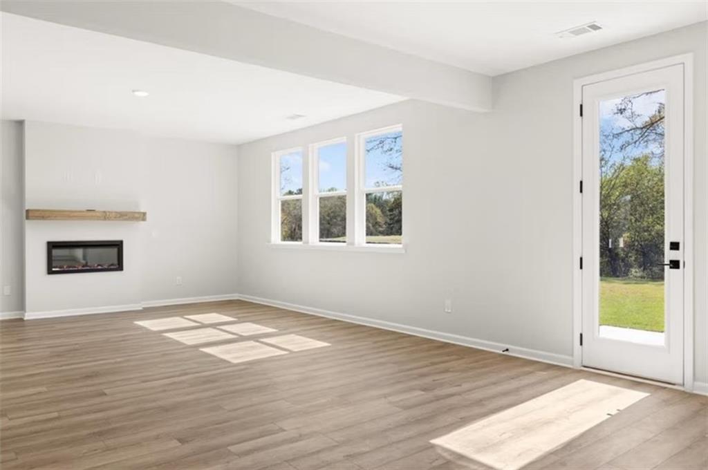 Bright living room with gas fireplace, hardwood floors, large windows, and glass door to lush backyard in The Hickory B, Cedar Farms, Winder GA