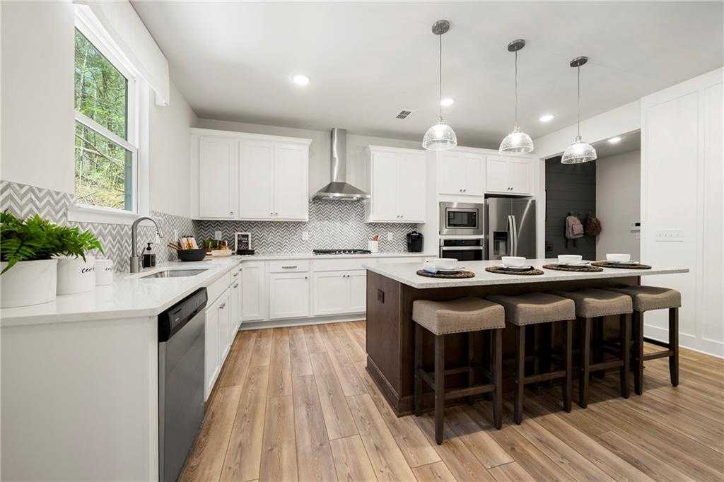 Modern white shaker kitchen with large island, stainless steel appliances, and hardwood floors in Davidson Homes The Hickory B, Dallas, GA
