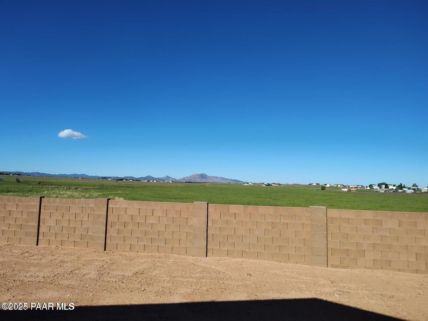 Scenic green pasture enclosed by tan block wall with distant mountains under blue sky in North Ridge at Pronghorn Ranch, Prescott Valley, Arizona