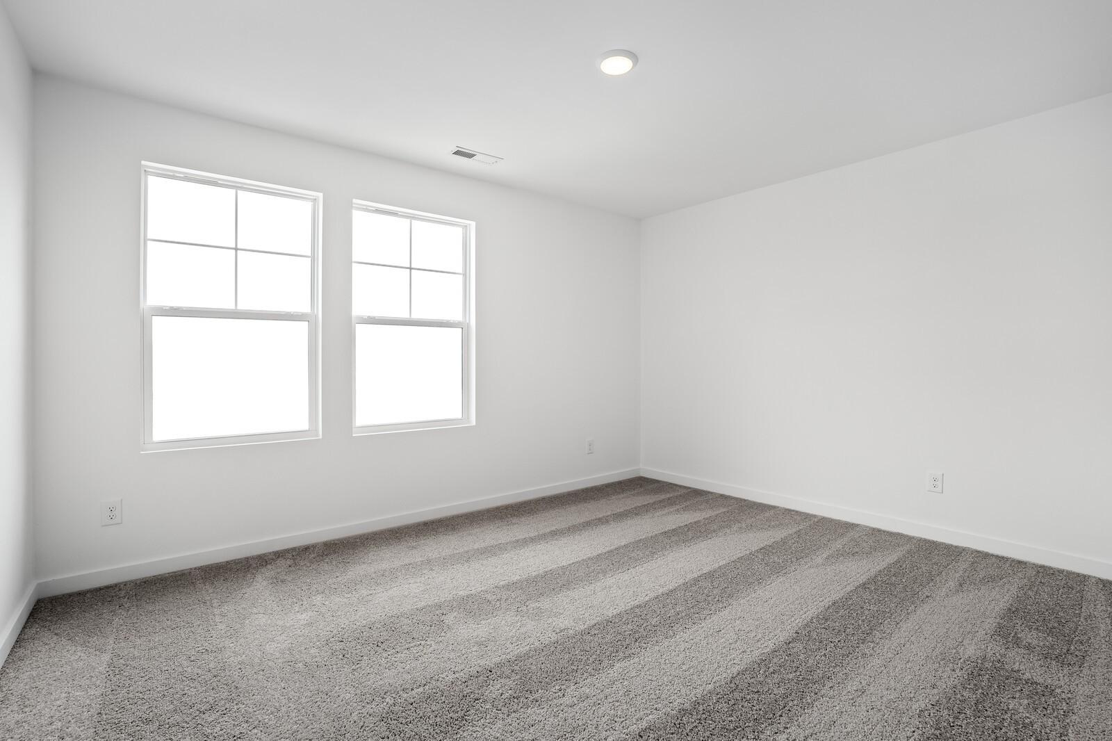 Bright empty bedroom with large windows, white walls, and striped neutral carpet in Davidson Homes The Logan C, White House, TN