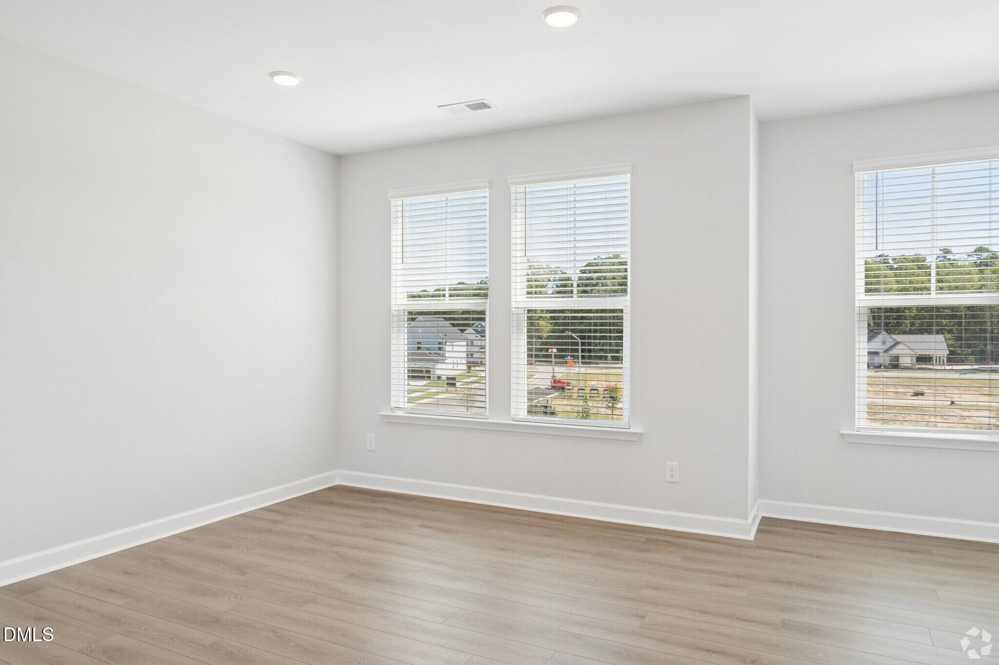 Bright empty room with luxury vinyl plank flooring, white walls, and windows with blinds in Davidson Homes' Mitchell floor plan, Knightdale.