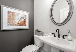 Modern powder room in The Washington H townhome with gray accent wall, abstract artwork, round mirror, and white pedestal sink