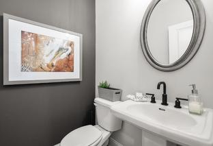 Modern powder room in The Washington H townhome with gray accent wall, abstract artwork, round mirror, and white pedestal sink