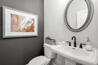 Modern powder room in The Washington H townhome with gray accent wall, abstract artwork, round mirror, and white pedestal sink