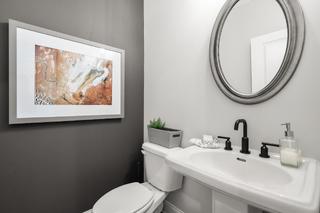 Modern powder room in The Washington H townhome with gray accent wall, abstract artwork, round mirror, and white pedestal sink