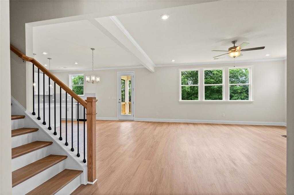 Open great room with hardwood floors, large windows, ceiling fan, and oak staircase in Davidson Homes The Hickory B at Wehunt Meadows, Hoschton