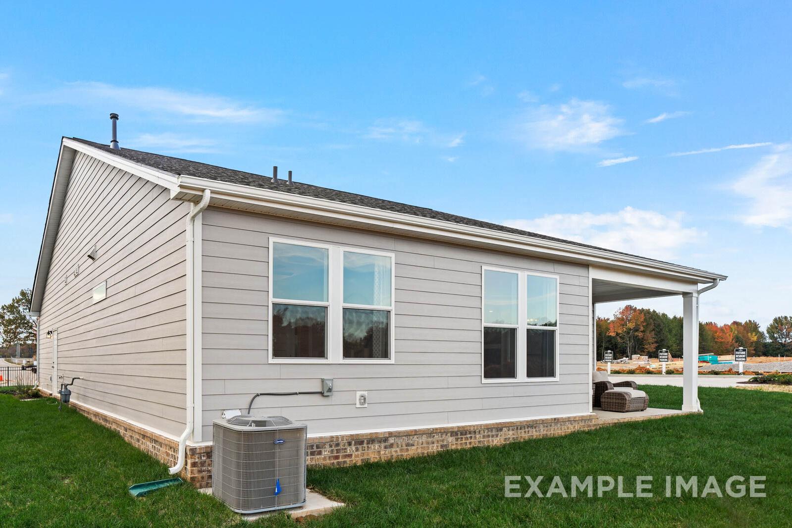 Side elevation of The Franklin B single-story home showcasing gray siding, large windows, covered porch with seating, AC unit, and green lawn