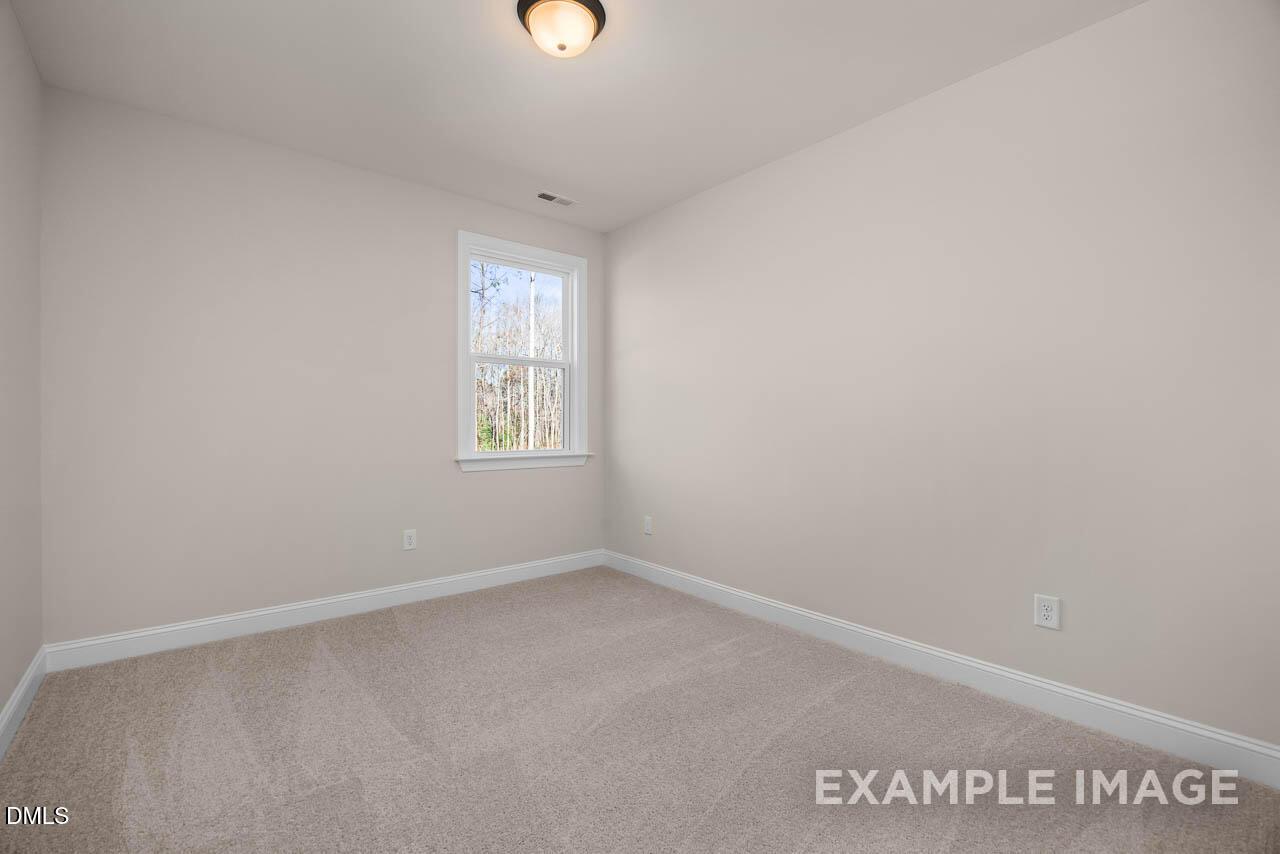 Spacious empty bedroom with beige walls, plush carpet, and window overlooking trees in Davidson Homes Crawford D, Angier, NC