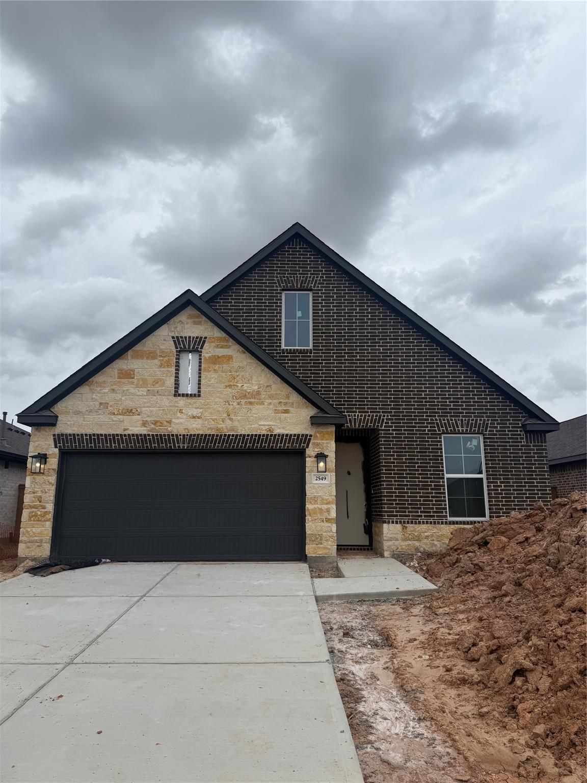 Modern one-story brick home with stone accents, black 2-car garage, and concrete driveway in Sunterra, Katy, Texas
