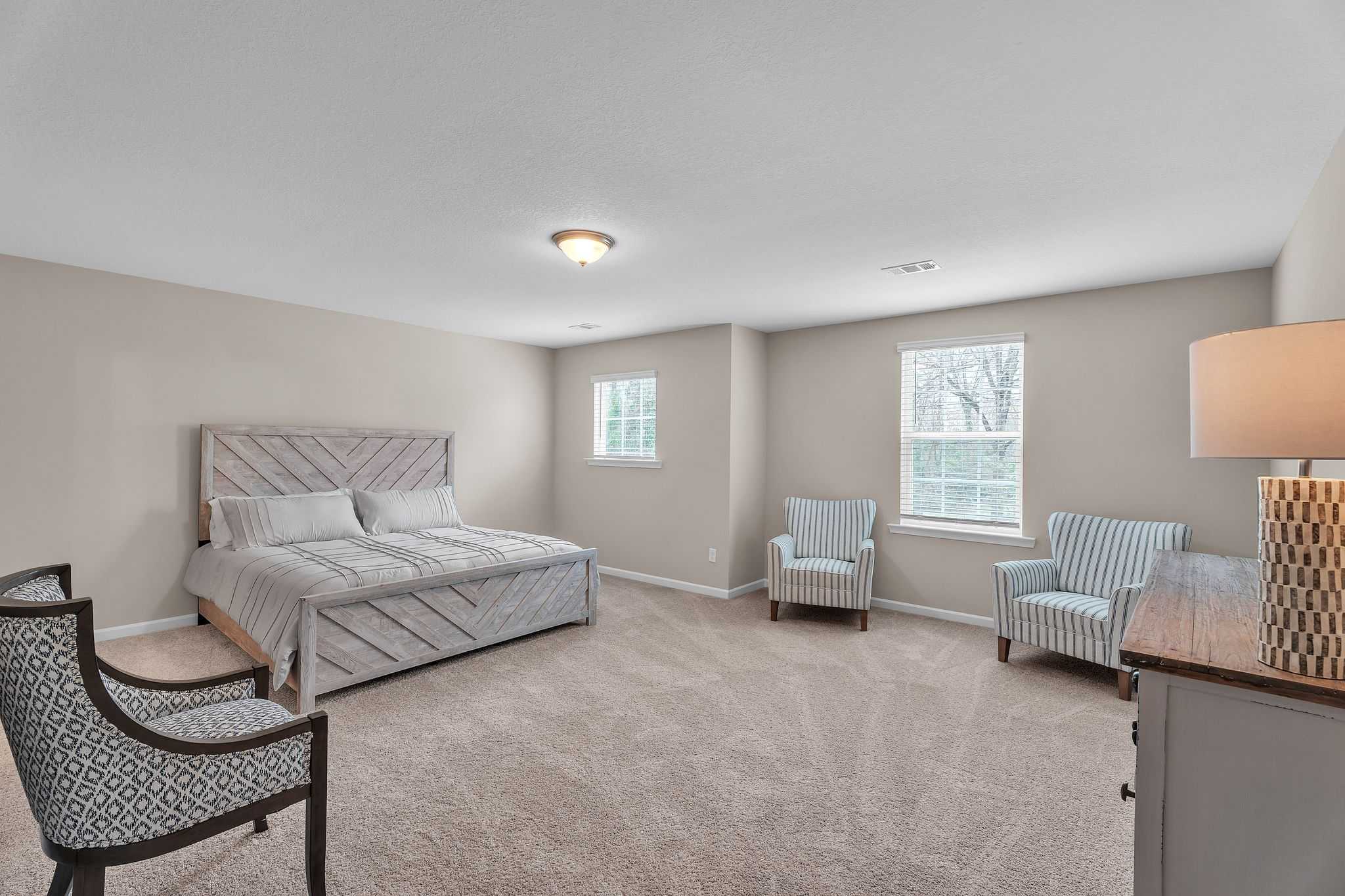 Spacious primary bedroom in Summer Vineyard, Phenix City AL with tufted king bed, accent chairs, and neutral decor by Davidson Homes