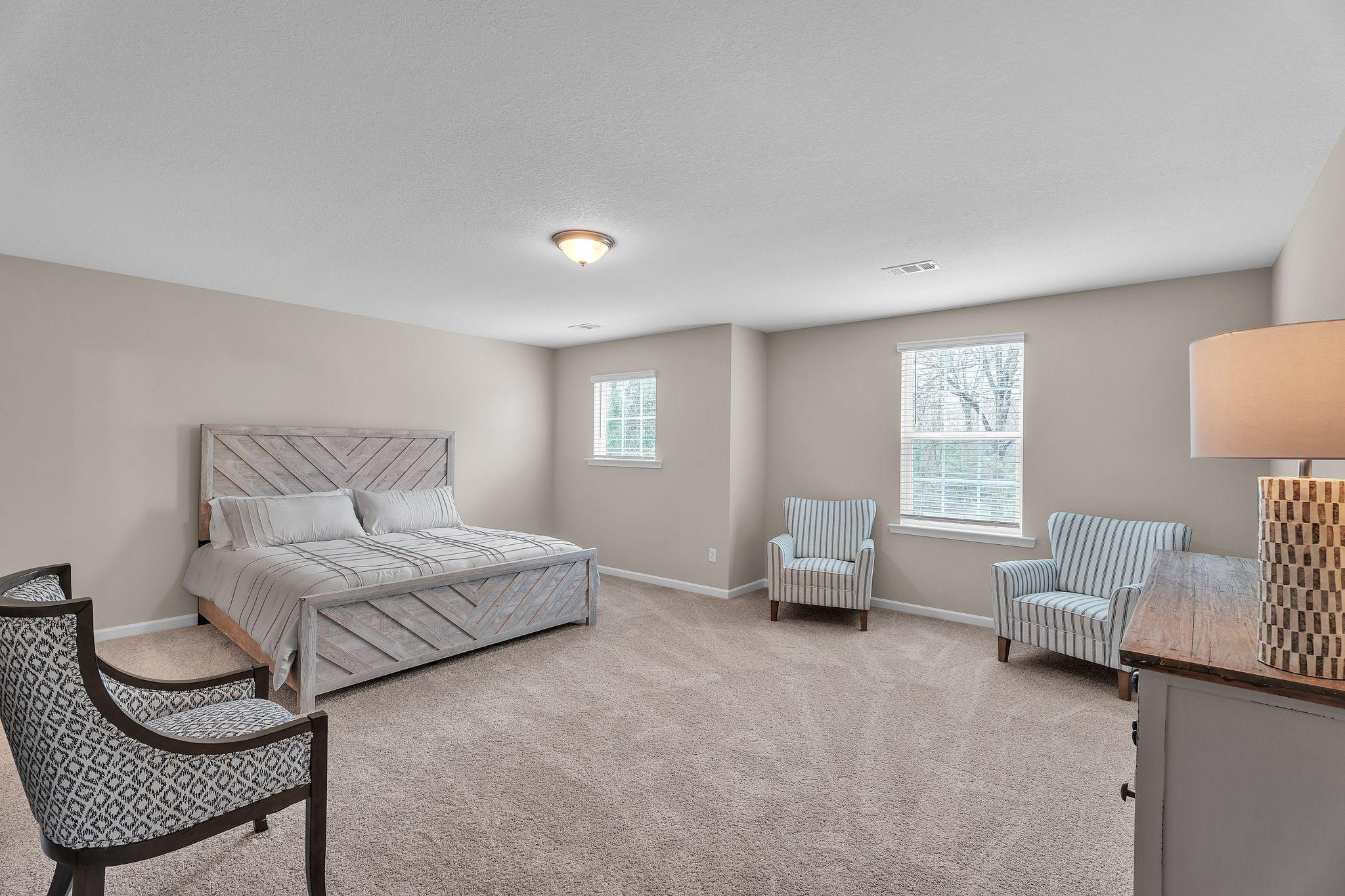 Spacious primary bedroom in Summer Vineyard, Phenix City AL with tufted king bed, accent chairs, and neutral decor by Davidson Homes