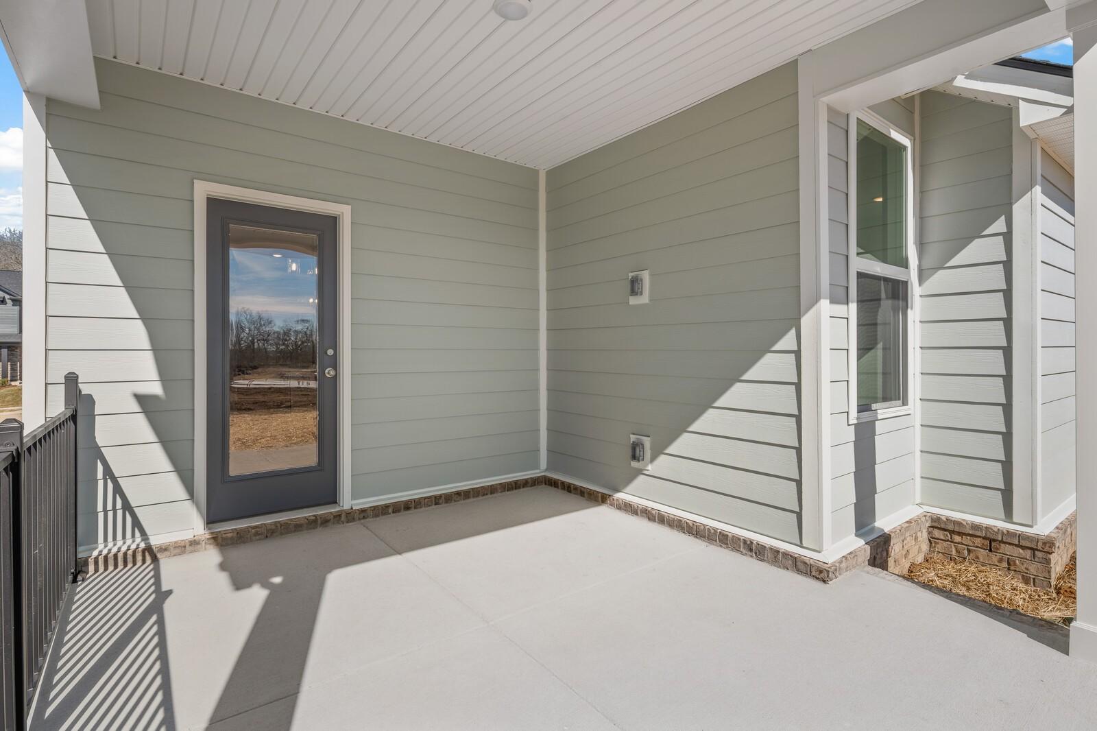 Covered back porch with sage green siding, glass door, and concrete patio in Davidson Homes The Ash A, Gallatin, TN