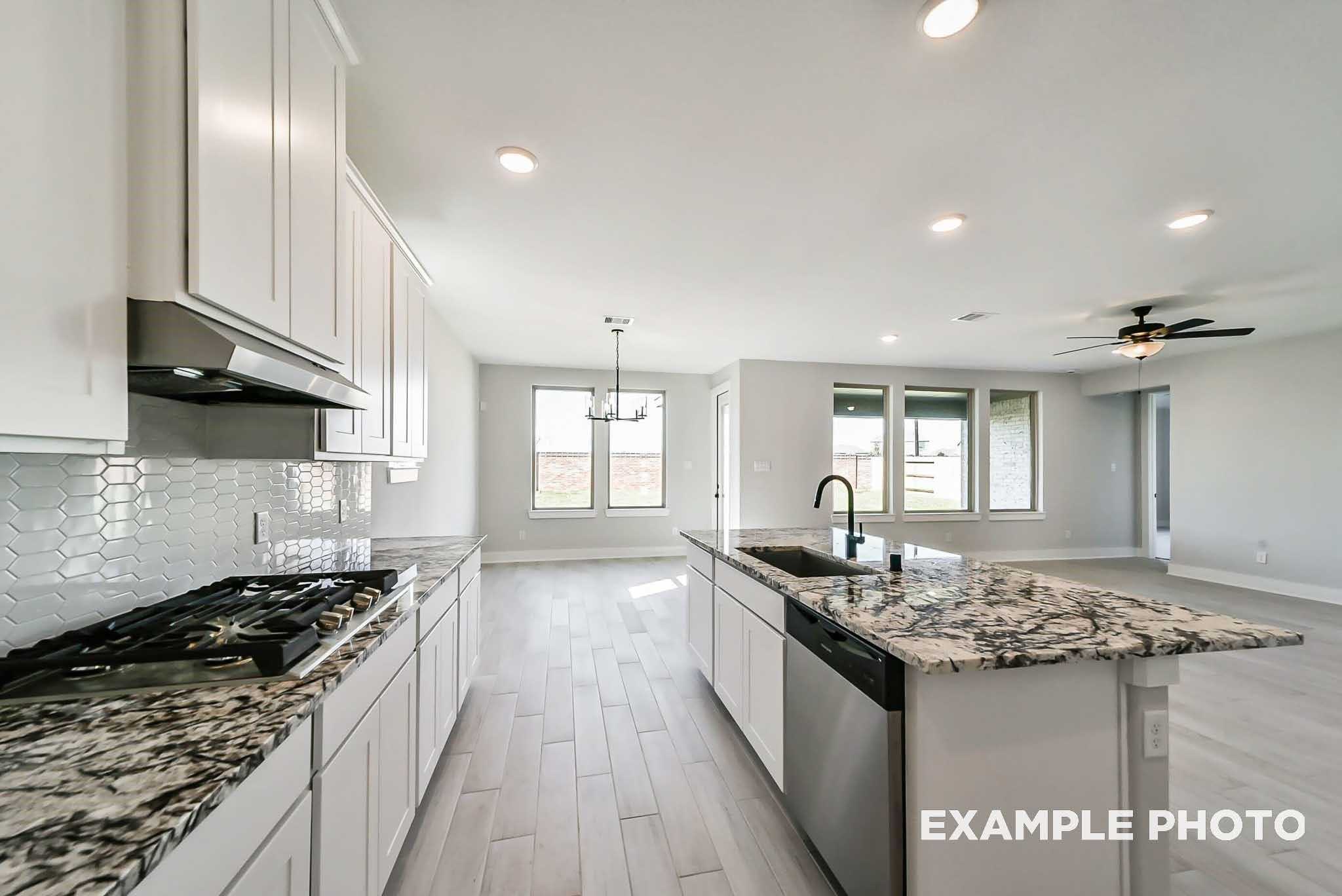 Modern open-concept kitchen with white cabinets, granite island sink, stainless appliances, and subway tile backsplash in 4-bedroom Davidson Homes The Philip C, Rosharon, Texas