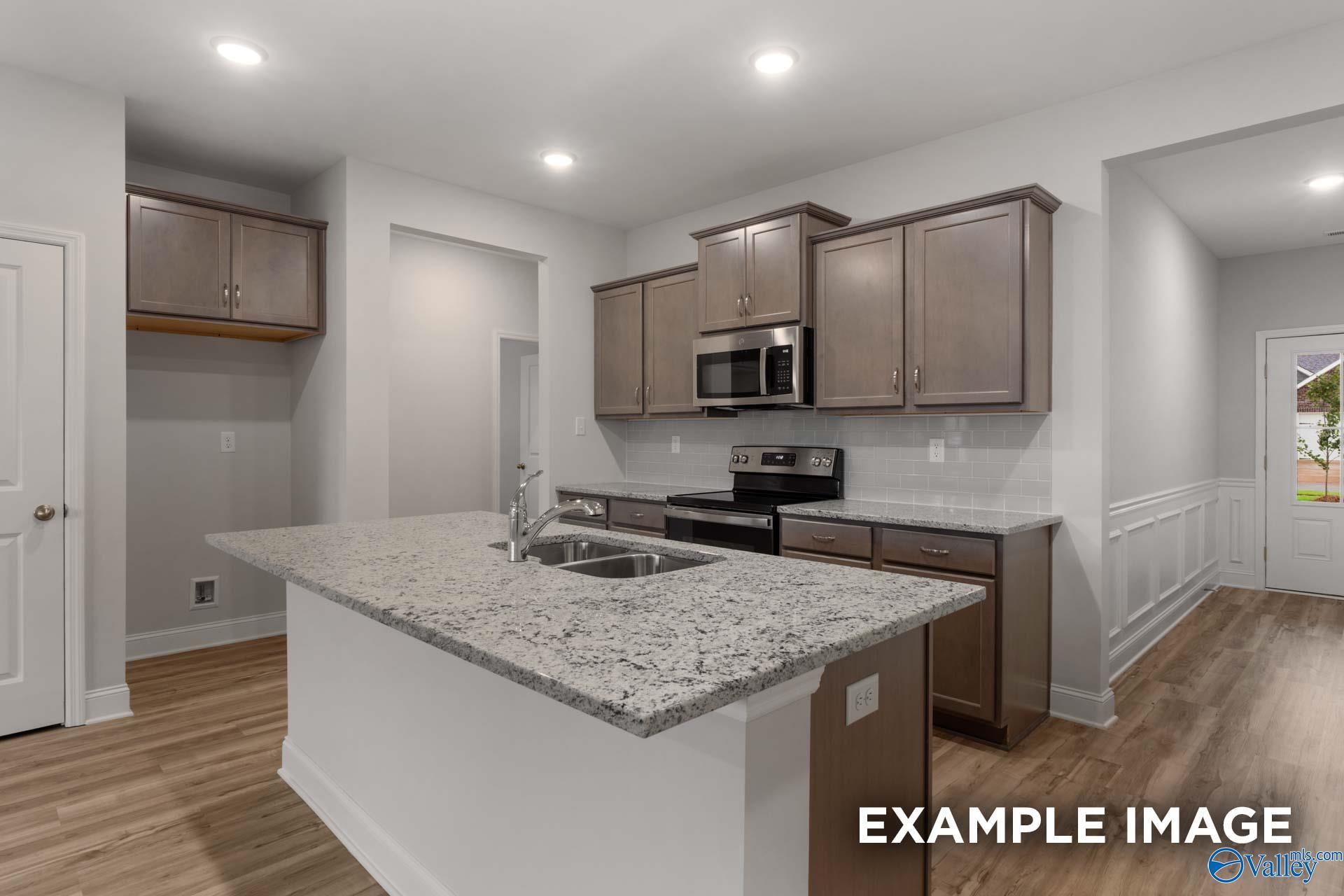 Modern kitchen with granite island sink, stainless steel appliances, and shaker cabinets in The Cumberland B by Davidson Homes, Decatur, AL