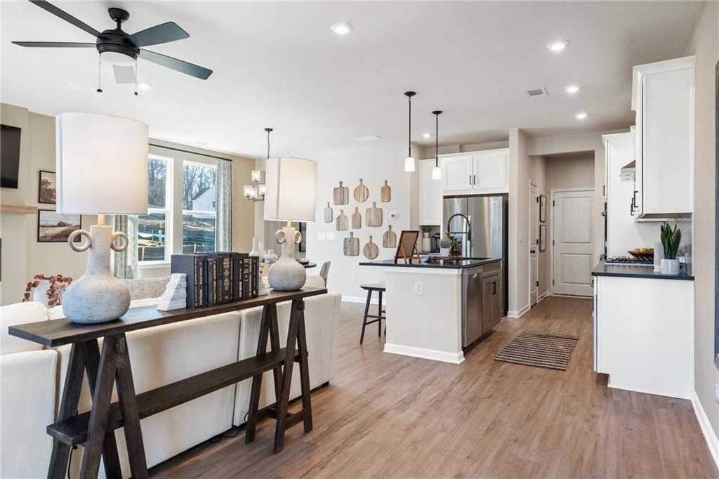 Open-concept living room and kitchen with white cabinets, stainless fridge, island seating, and hardwood floors in The Marion C, Winder, GA