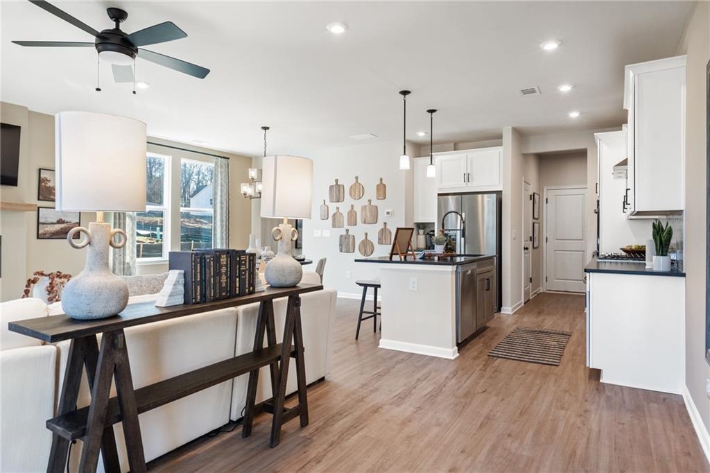 Open-concept living room and kitchen with white cabinets, stainless fridge, island bar, and hardwood floors in The Marion B, Kennesaw, GA