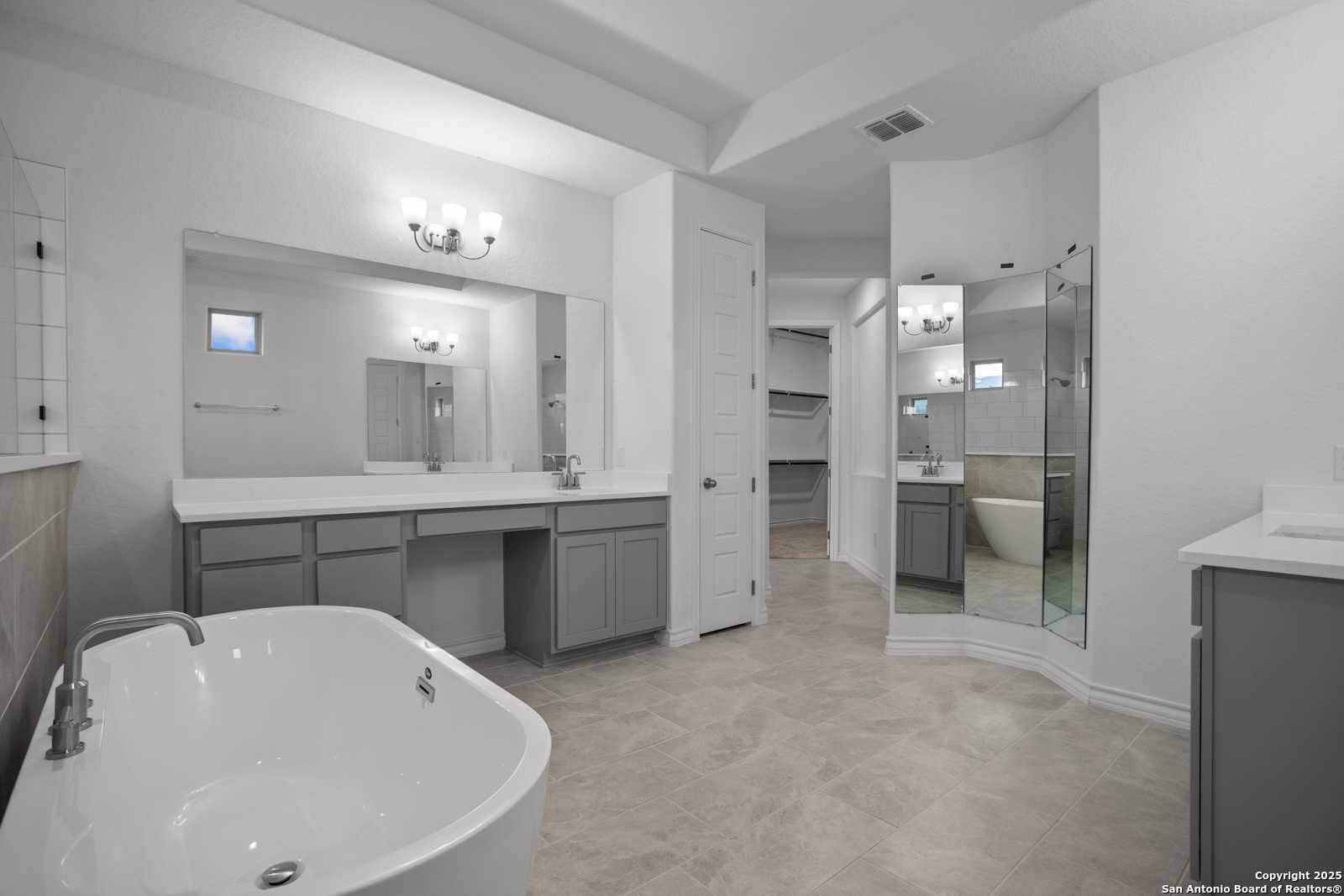 Luxurious master bathroom featuring freestanding tub, double vanity with gray cabinets, and mirrors in Davidson Homes The Summerlin B, Castroville, Texas