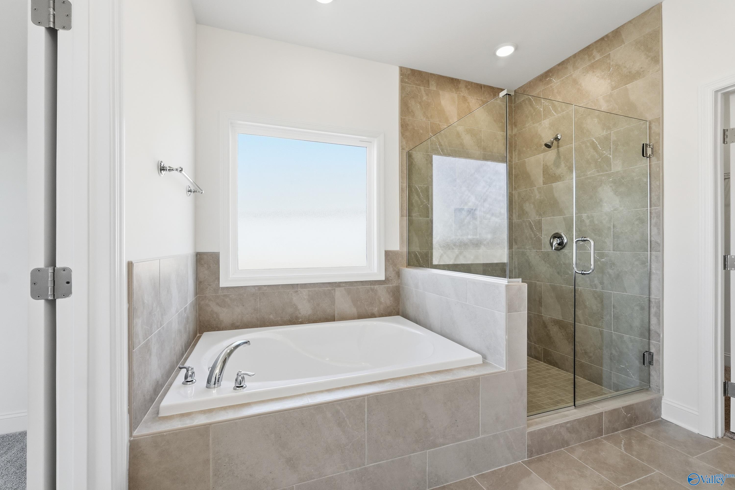 Elegant master bathroom with soaking tub, frameless glass shower, and tiled accents in Davidson Homes The Montgomery, Meridianville, AL