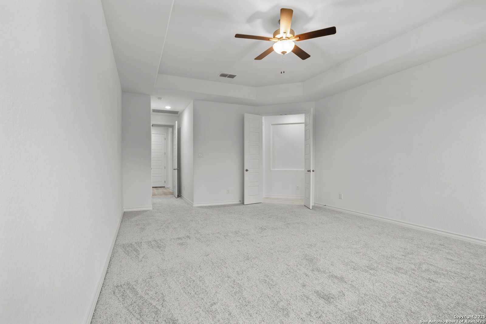 Spacious bedroom with ceiling fan, white walls, carpet floor, and open double doors to closet in Davidson Homes The Summerlin B, Castroville, Texas