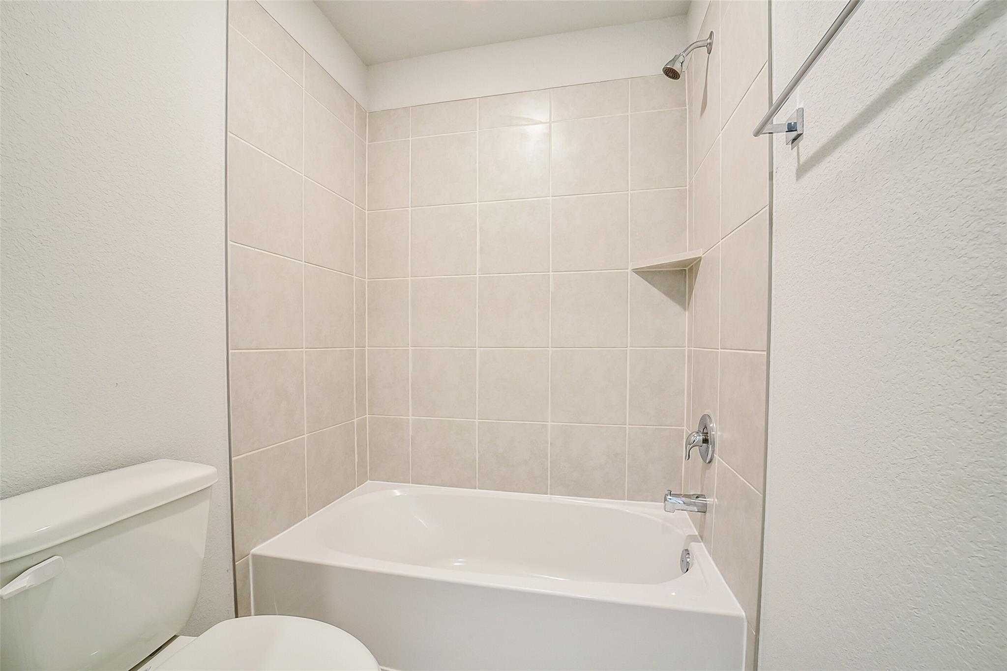 Modern bathroom with bathtub-shower combo, neutral tile walls, and white fixtures in Davidson Homes The Blanco E, Magnolia Texas