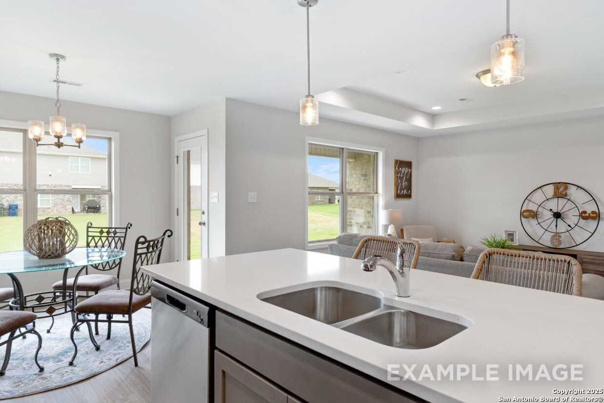 Modern open-concept kitchen with white island sink, glass dining table, and pendant lights in The Asheville K by Davidson Homes, Bricewood, San Antonio