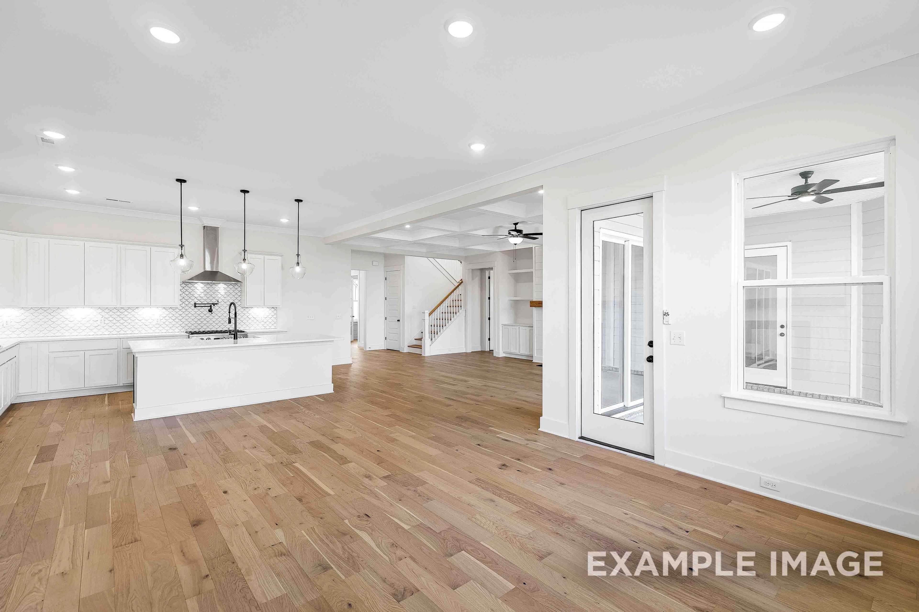 Open-concept kitchen in The Albany A with white shaker cabinets, large island, stainless appliances, hardwood floors, and adjacent living space