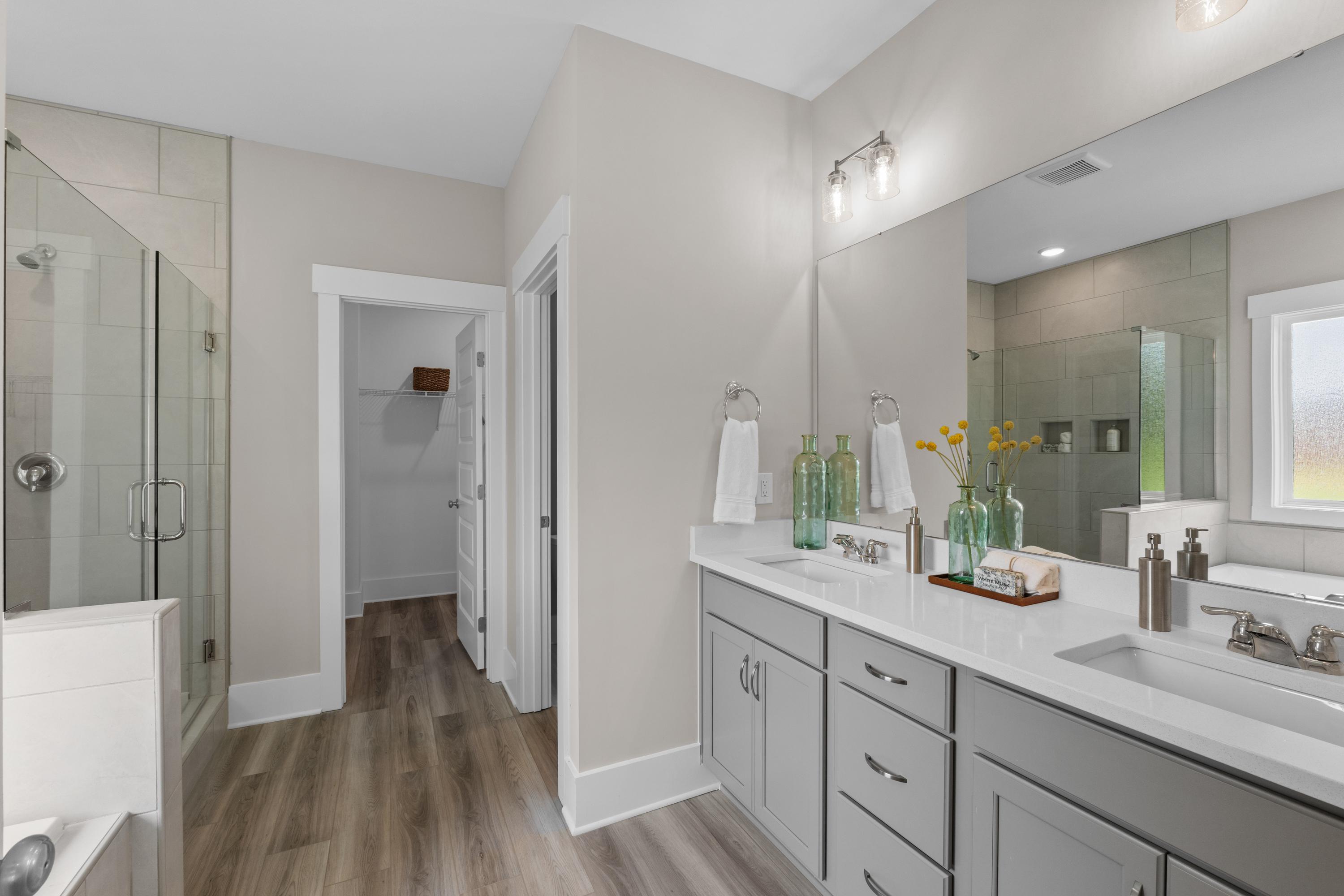 Spacious master bathroom in The Highlands Arab Alabama with dual gray vanities, walk-in glass shower, and light wood floors