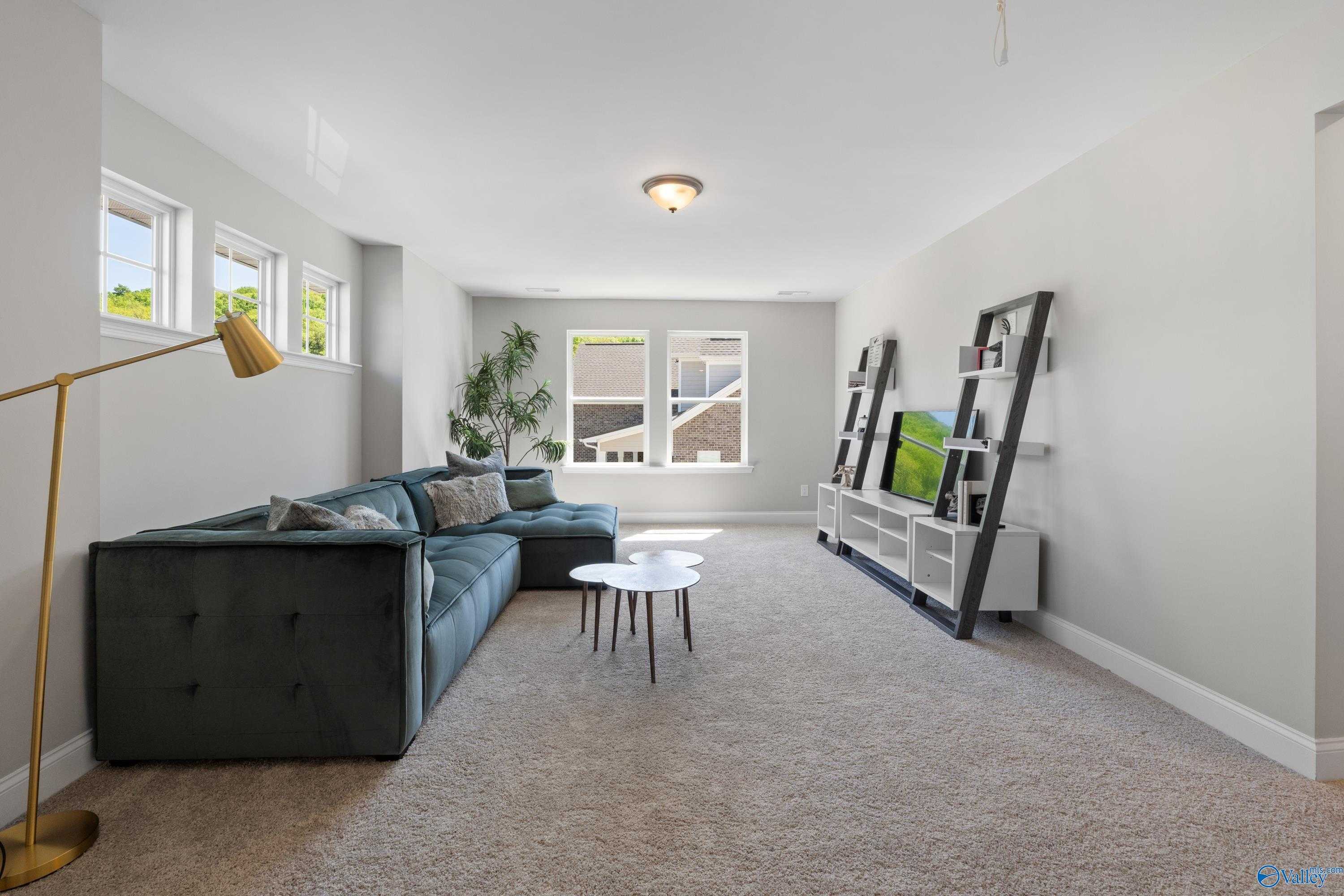 Spacious upstairs loft with green velvet sectional sofa, TV console, potted plants, and large windows in Evermore Homes The Haven, Owens Cross Roads