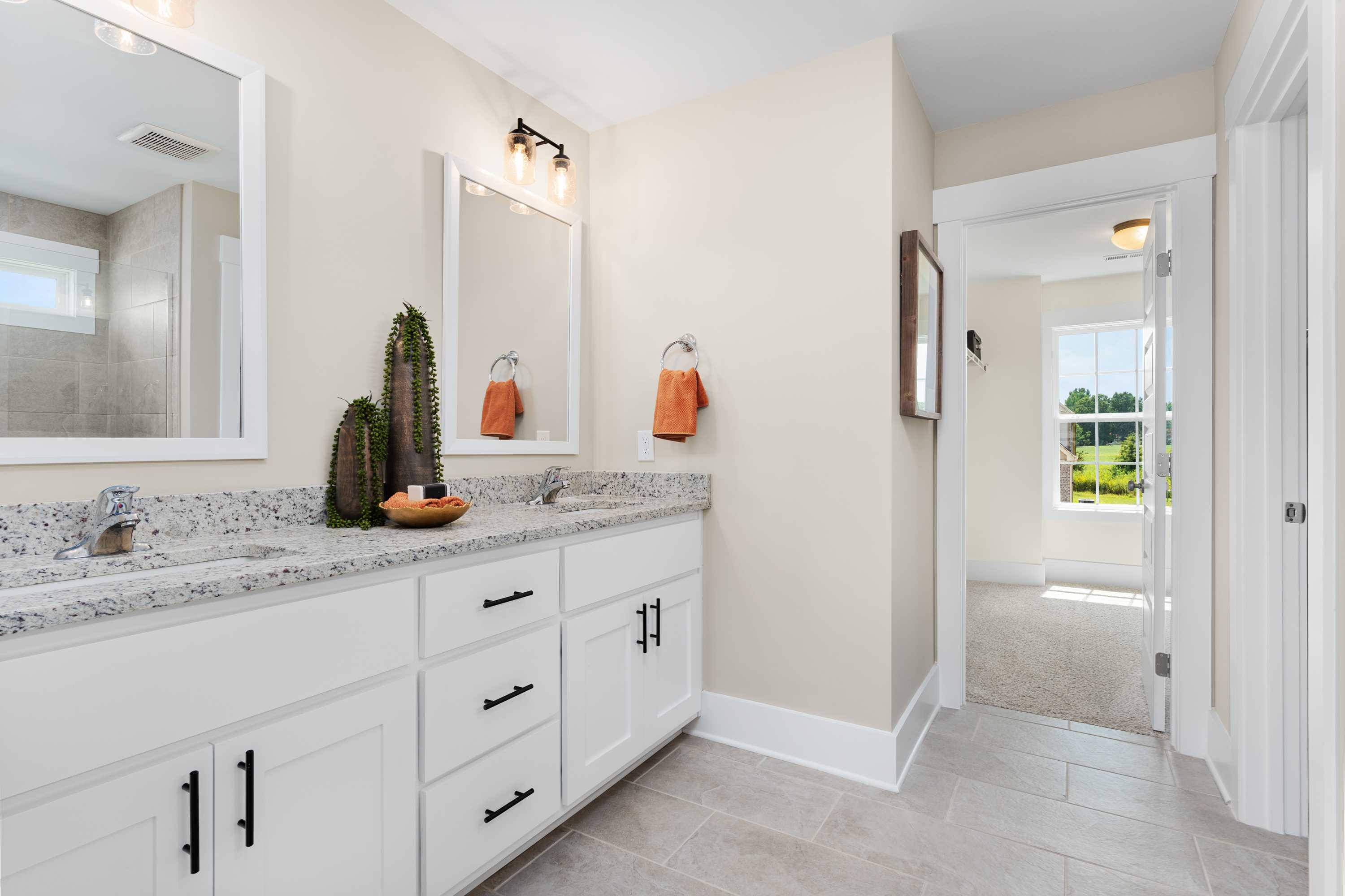 Spacious master bathroom in The Shelby A featuring double vanity with white cabinets, quartz counters, and orange accents