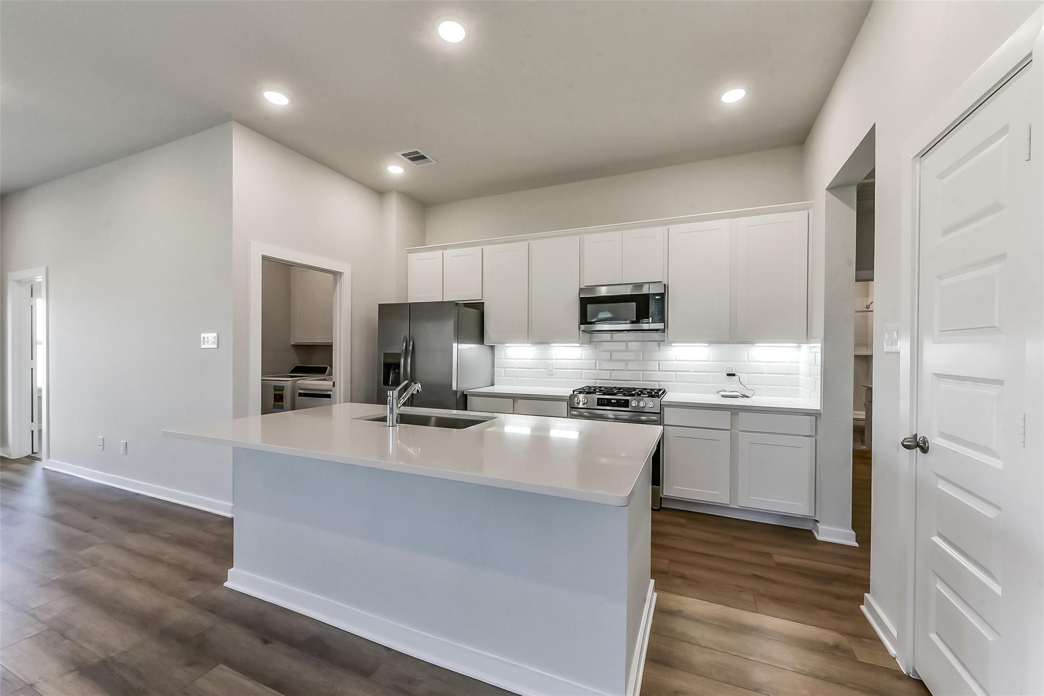 Modern white kitchen with quartz island, stainless appliances, subway tile backsplash in Davidson Homes The Costa C, Dayton, Texas