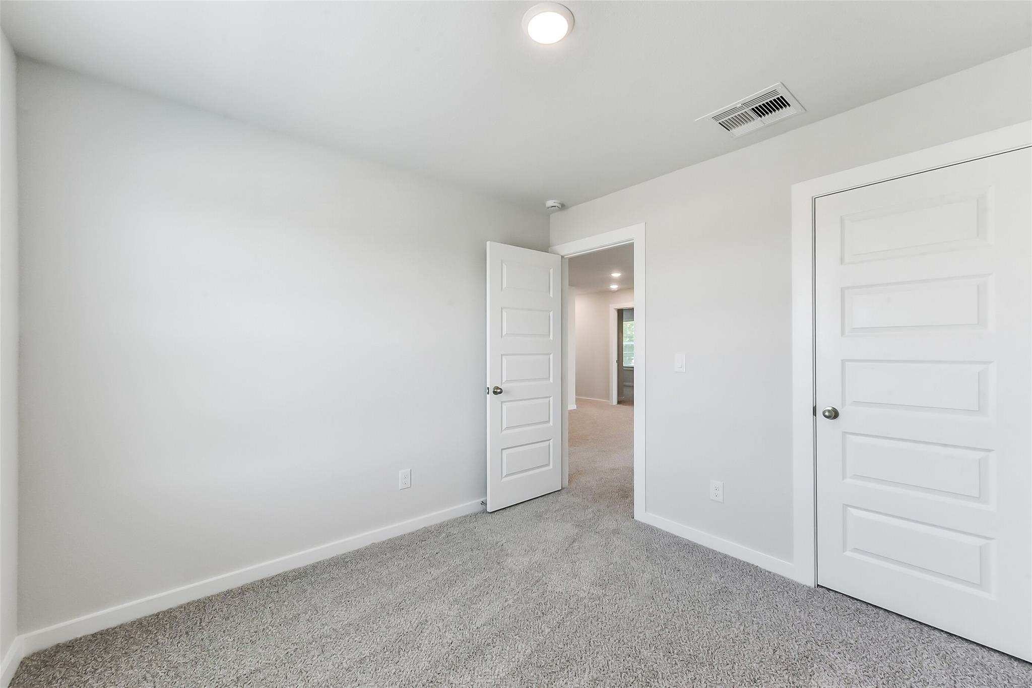 Empty bedroom with gray carpet, white walls, and open door to hallway in The Brazos E 5-bedroom home, Magnolia, Texas