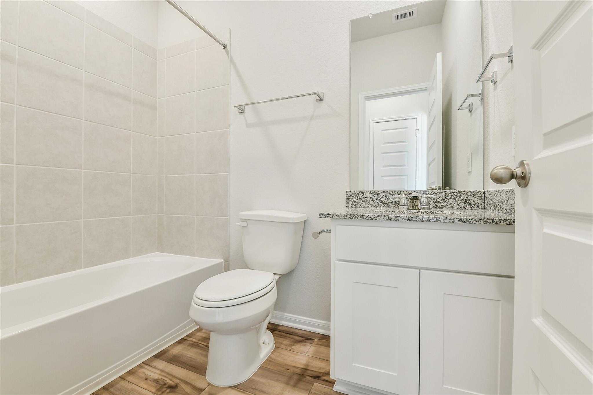 Modern bathroom with granite vanity, white subway tile, bathtub, and toilet in Davidson Homes The Sabine E, Conroe, Texas