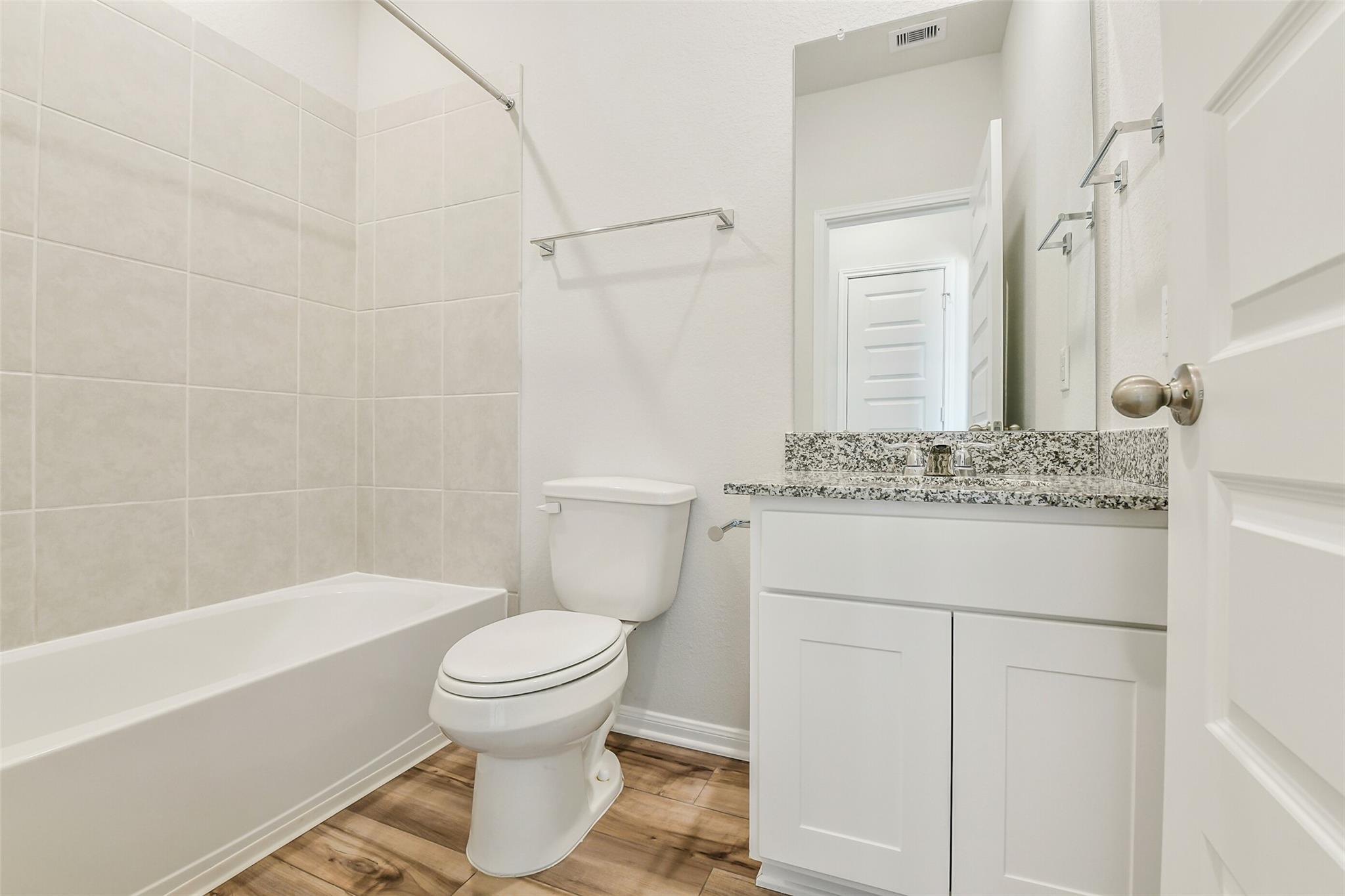 Modern bathroom with granite vanity, white subway tile, bathtub, and toilet in Davidson Homes The Sabine E, Conroe, Texas