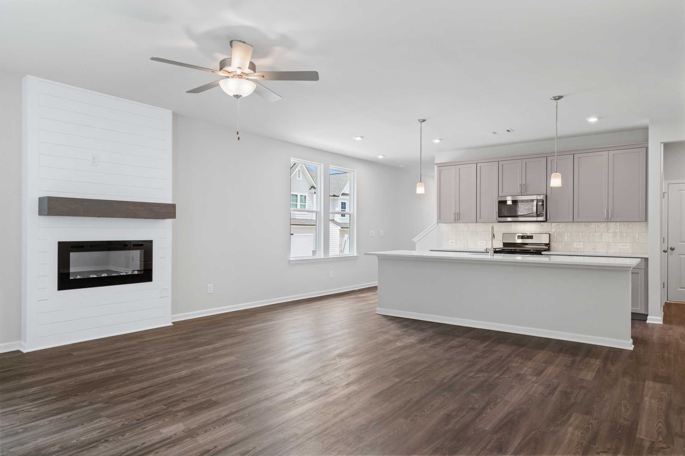Open-concept living room and kitchen in The Cary A with shiplap fireplace, white island, and hardwood floors