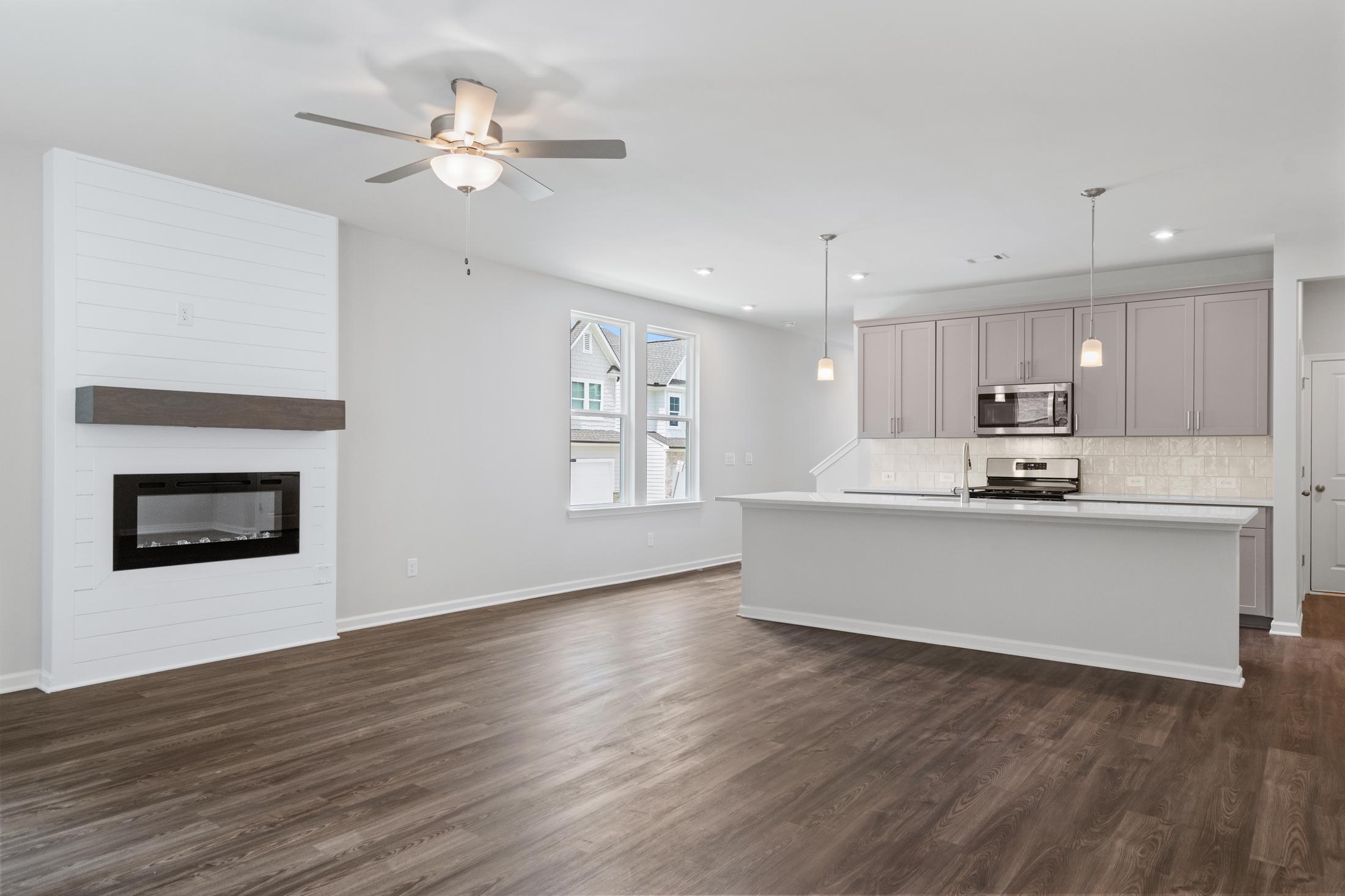 Open-concept living room and kitchen in The Cary A with shiplap fireplace, white island, and hardwood floors