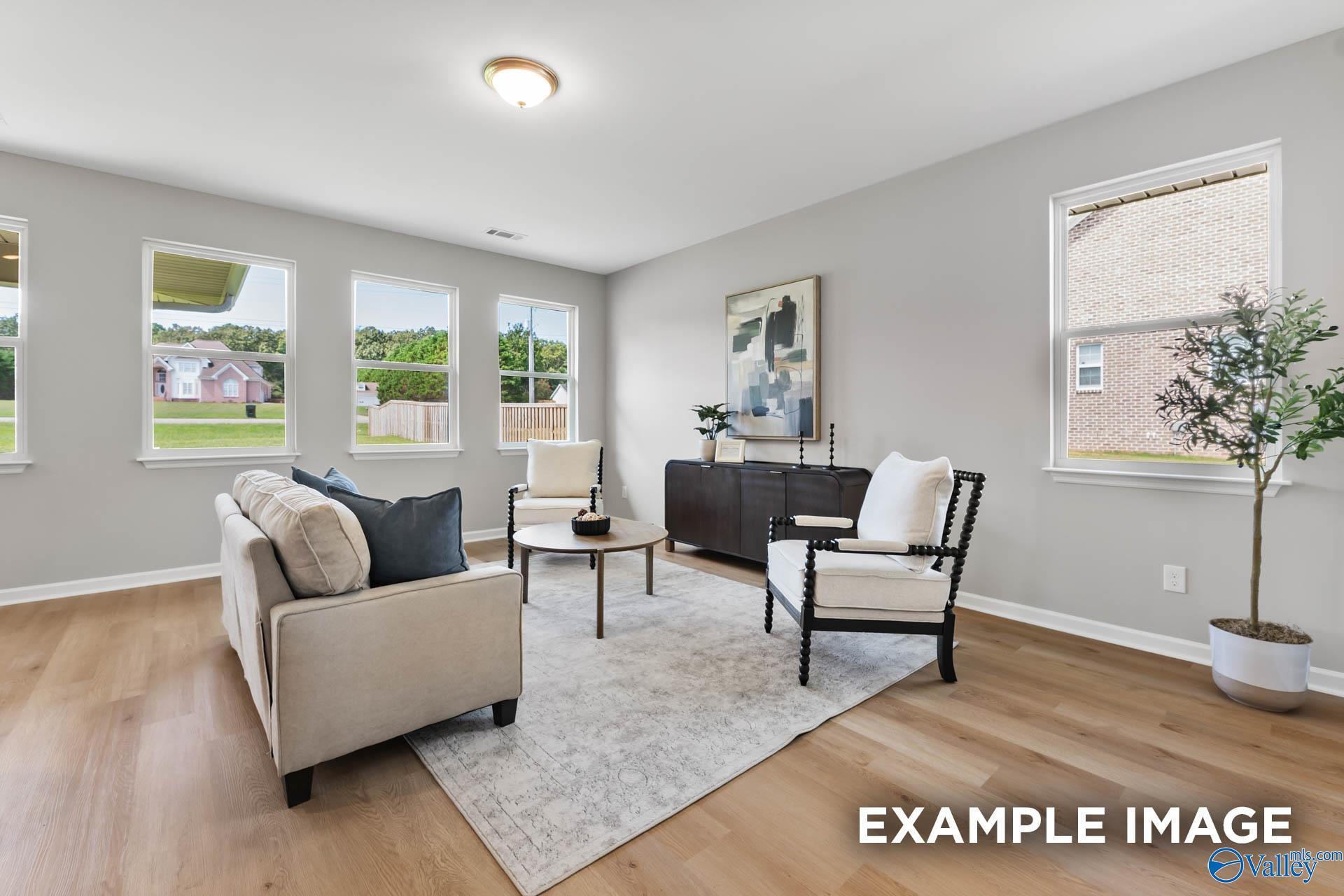 Cozy living room with beige sofa, armchairs, abstract art, and large windows in Davidson Homes The Charm, Huntsville, Alabama