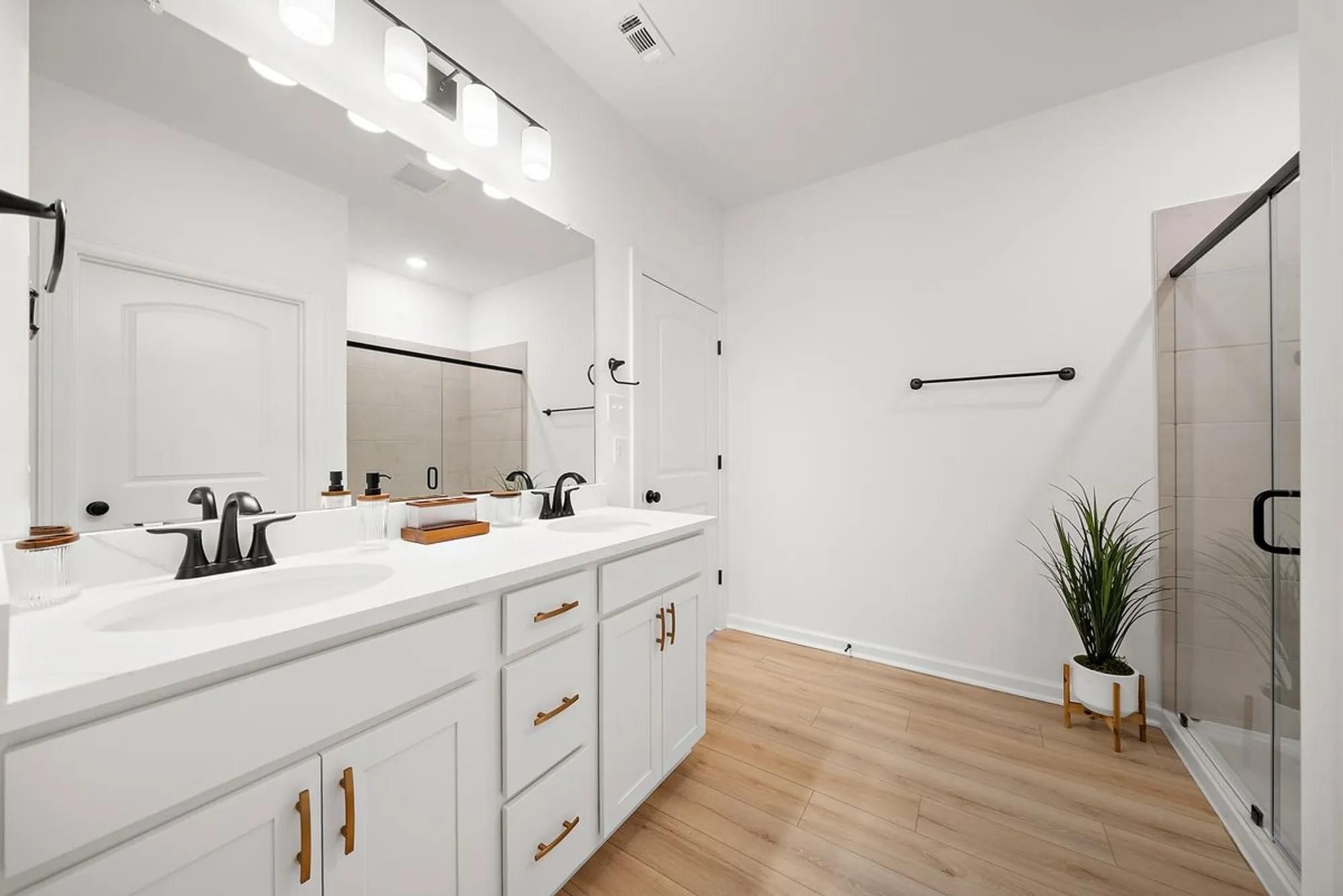 Modern primary bathroom featuring double vanity with white quartz, frameless glass shower, and hardwood floors in Davidson Homes The Luna L, Katy, Texas