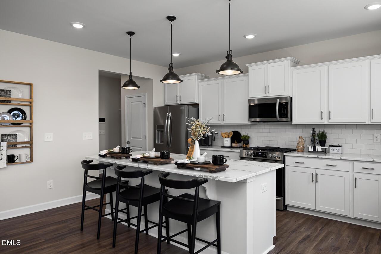 Modern kitchen with white shaker cabinets, stainless appliances, quartz island, and pendant lights in 5-bedroom Davidson Homes The Hickory II B, Zebulon, NC