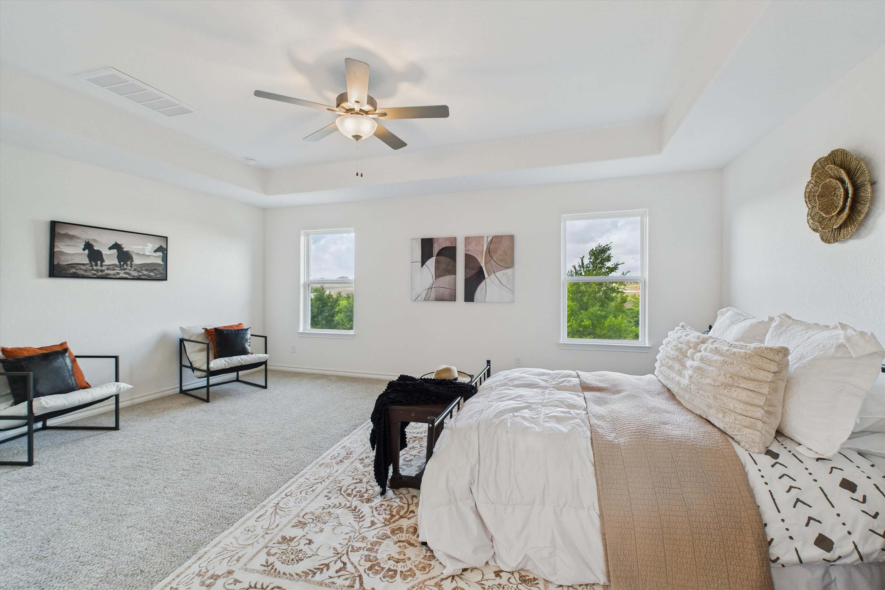 Spacious master suite in The Danbury with tray ceiling, neutral decor, and large windows in Castroville, Texas home.