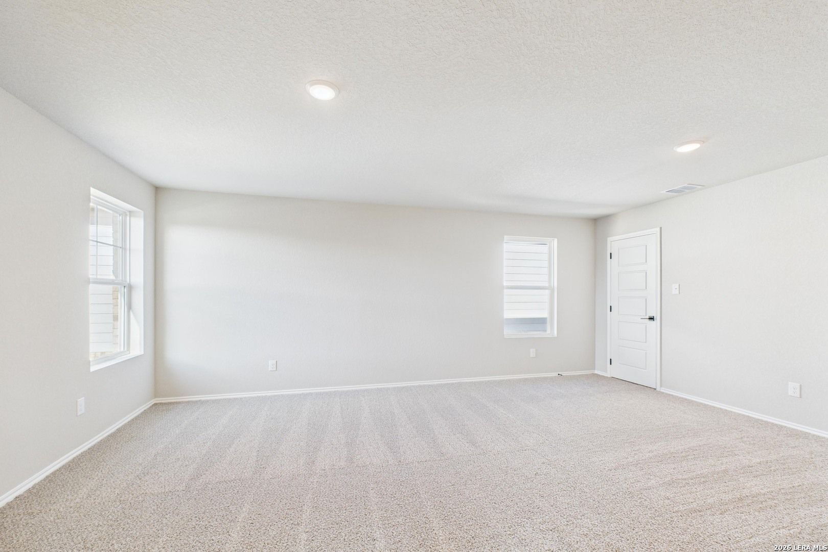Spacious empty bedroom with beige carpet, neutral walls, double windows, and closet door in Davidson Homes The Douglas E, Bricewood San Antonio