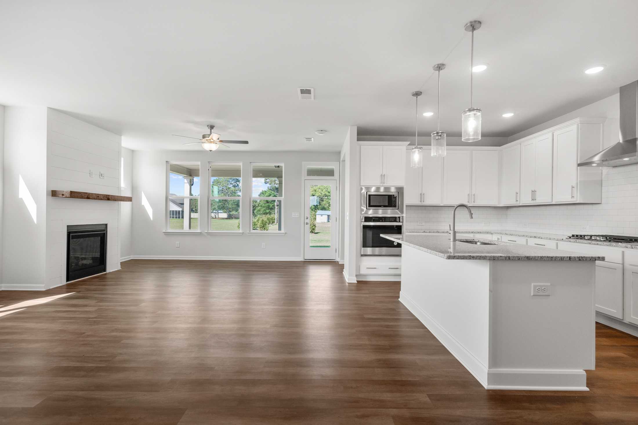 Spacious open-concept kitchen and living room at The Everleigh in Locust Grove GA with white cabinets, island, fireplace, hardwood floors