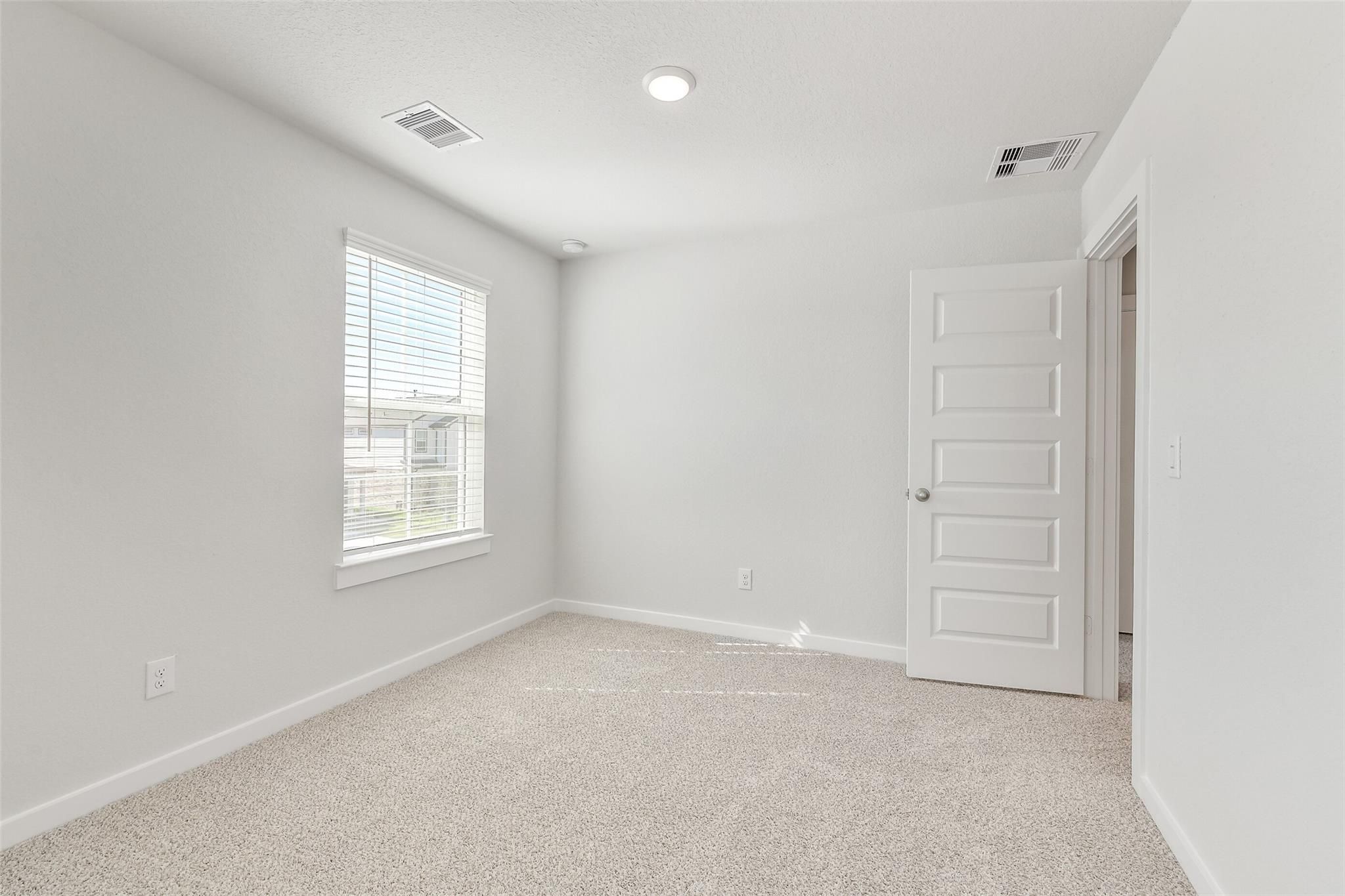 Bright secondary bedroom with light gray walls, beige carpet, and window blinds in Davidson Homes The Blanco E, Magnolia Texas