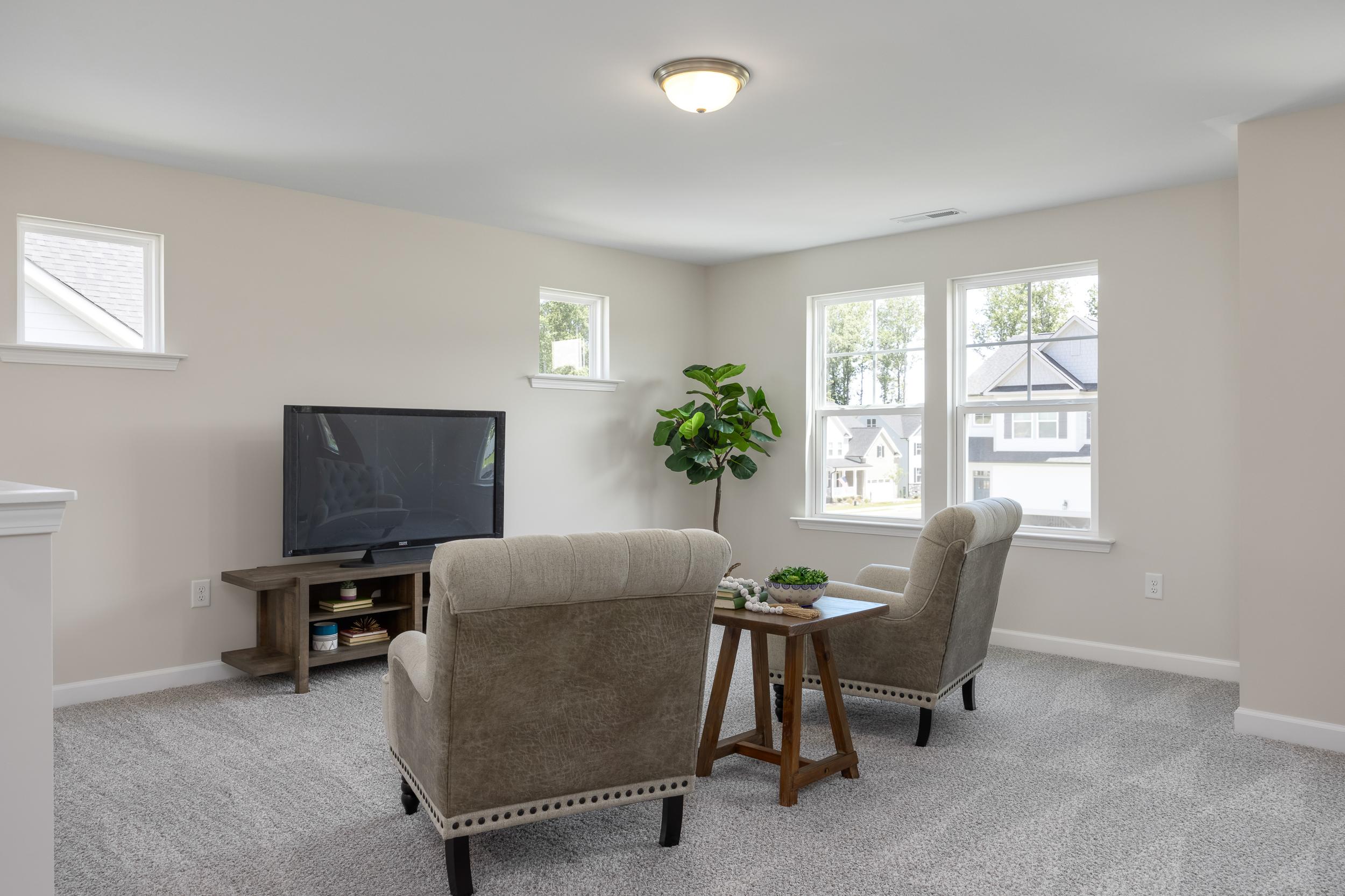 Cozy beige seating area at Montrose in Aberdeen NC with armchairs, wooden side table, TV console, and potted plant