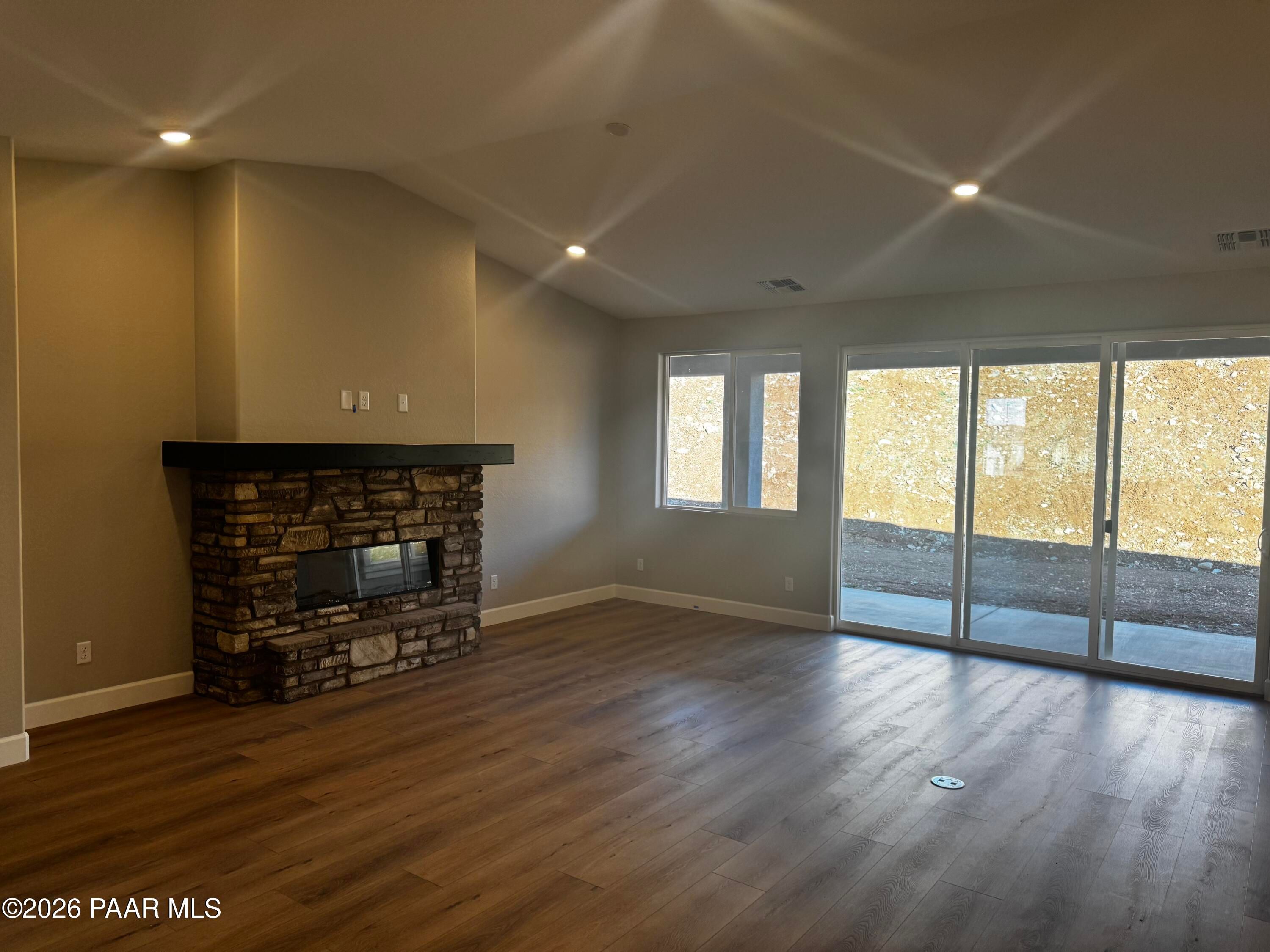 Cozy living room featuring stacked stone fireplace, hardwood floors, and sliding glass doors in Evermore Homes The Monarch B, Prescott Valley, Arizona