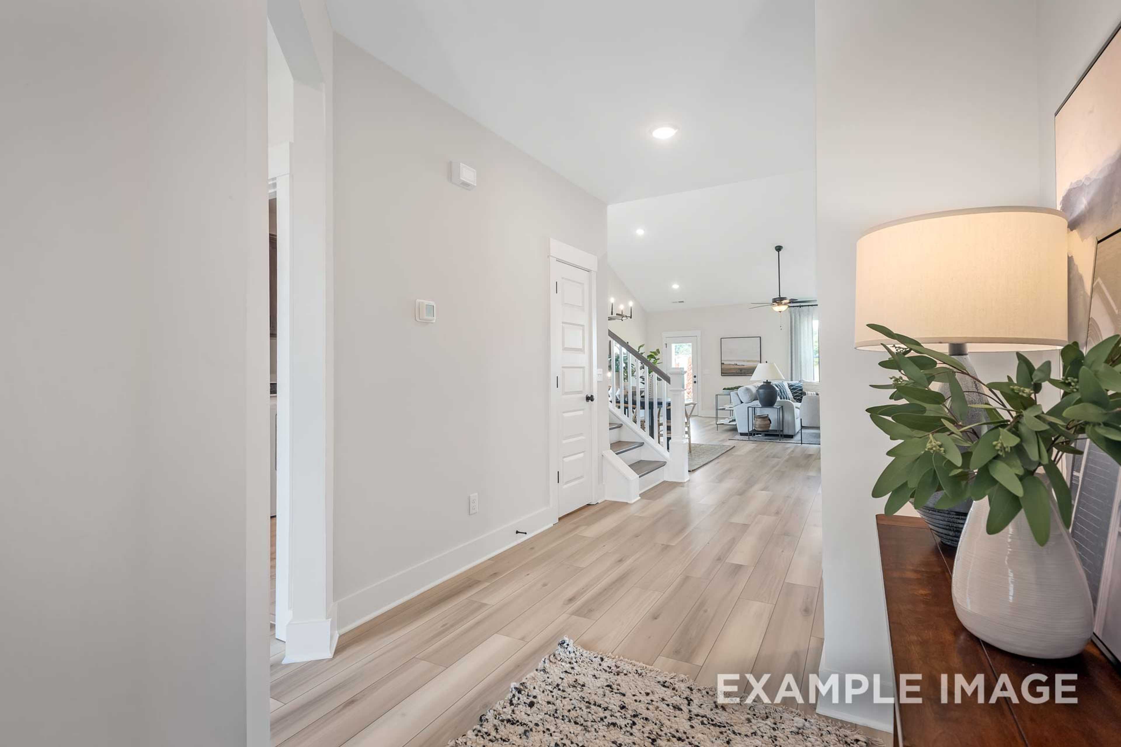 Spacious open foyer in The Ridgeport B showcasing light hardwood floors, white staircase, and adjacent living area