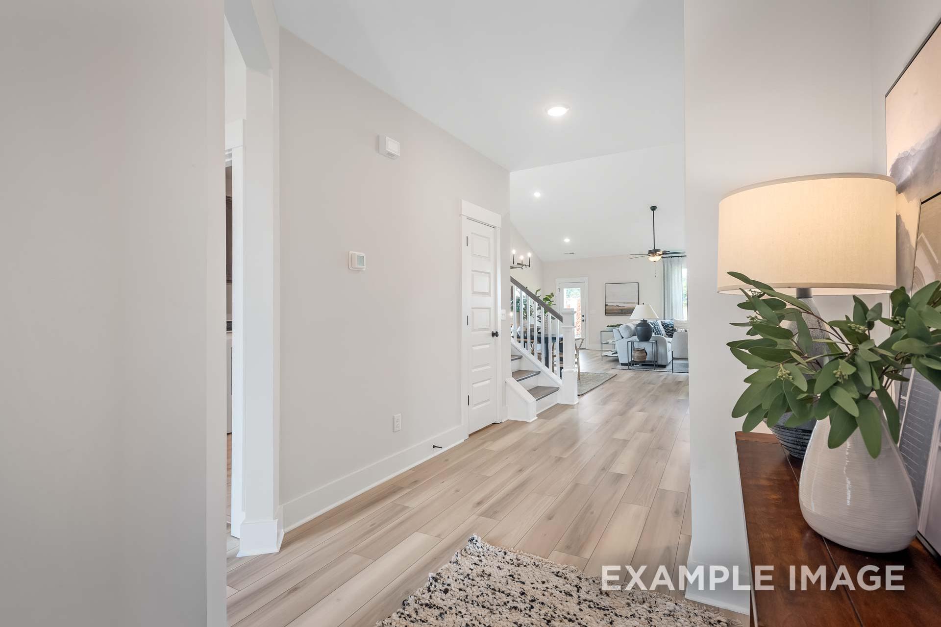 Spacious open foyer in The Ridgeport B showcasing light hardwood floors, white staircase, and adjacent living area