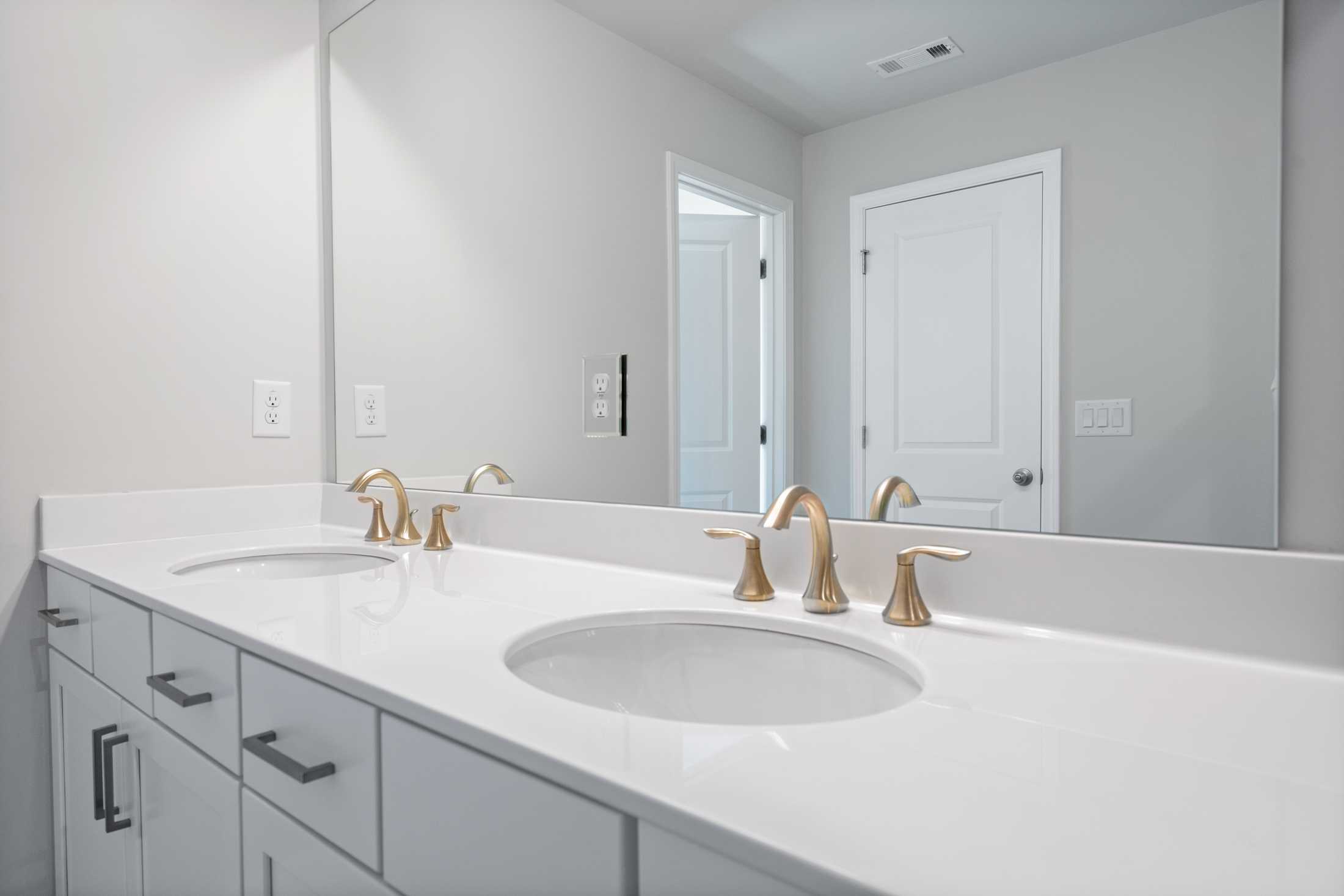 Elegant double vanity in The Cary A master bathroom with gold faucets, white sinks, and quartz countertop