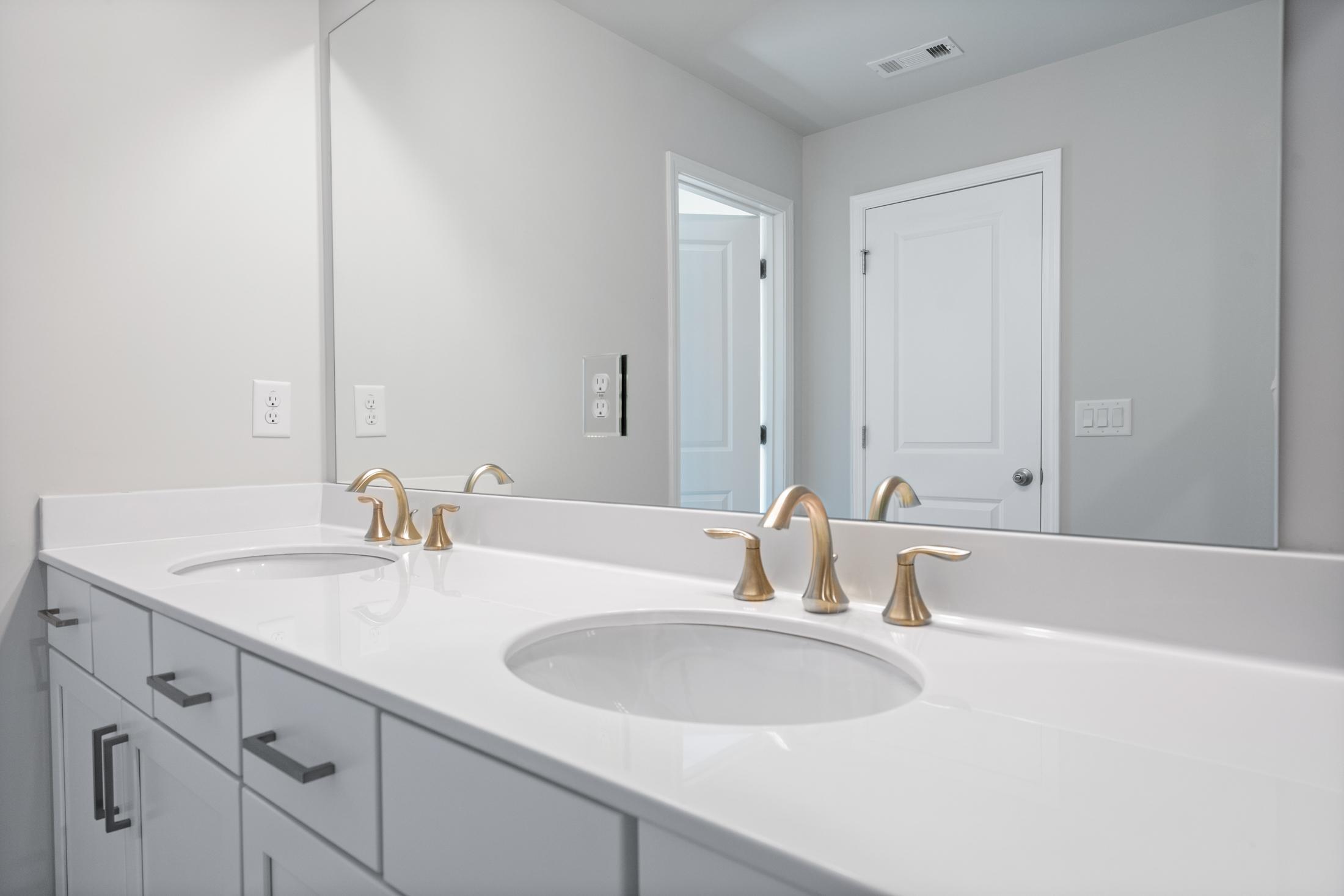 Elegant double vanity in The Cary A master bathroom with gold faucets, white sinks, and quartz countertop