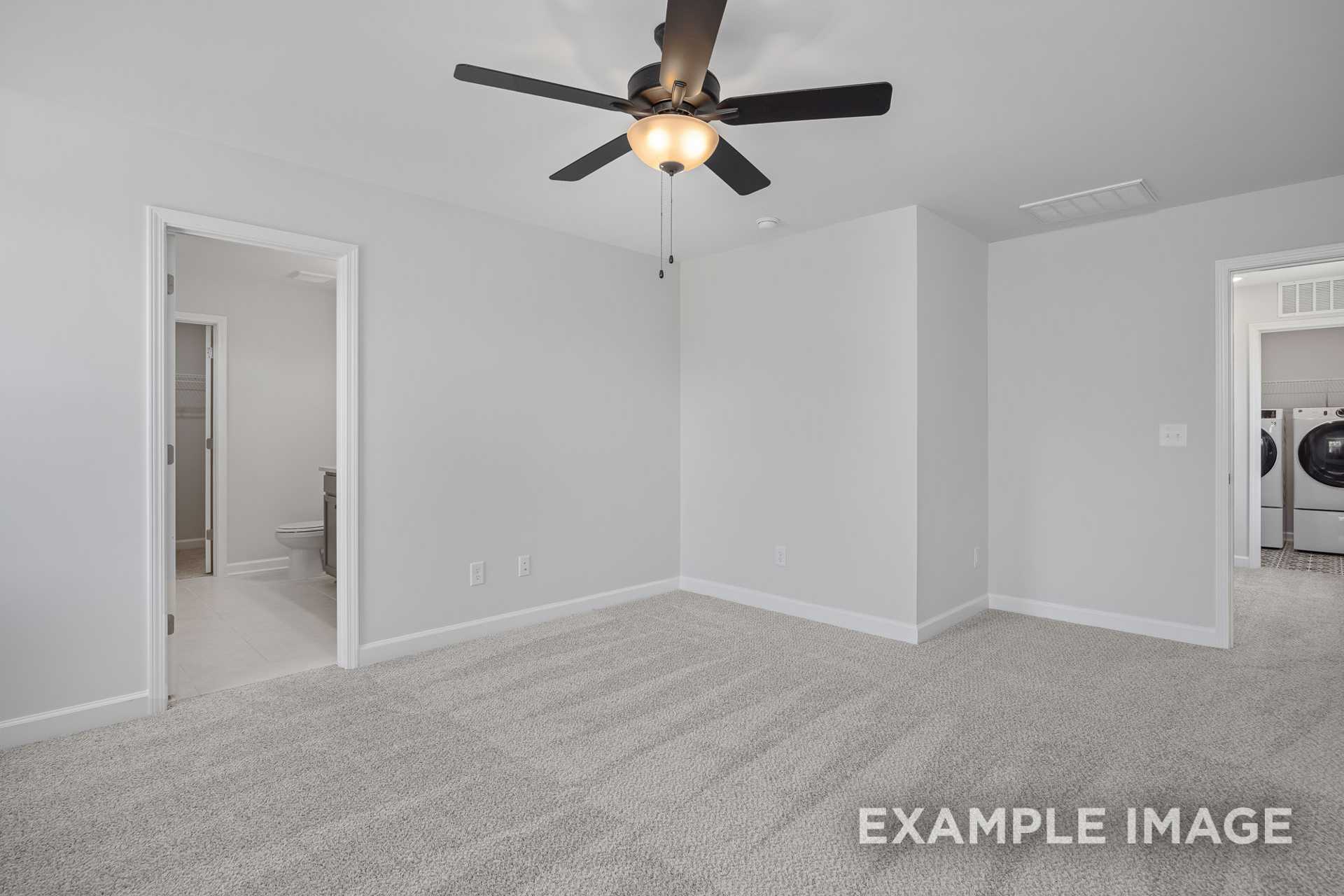 Spacious upper-floor master bedroom in The Grace C with gray carpet, ceiling fan, white walls, and adjacent laundry room