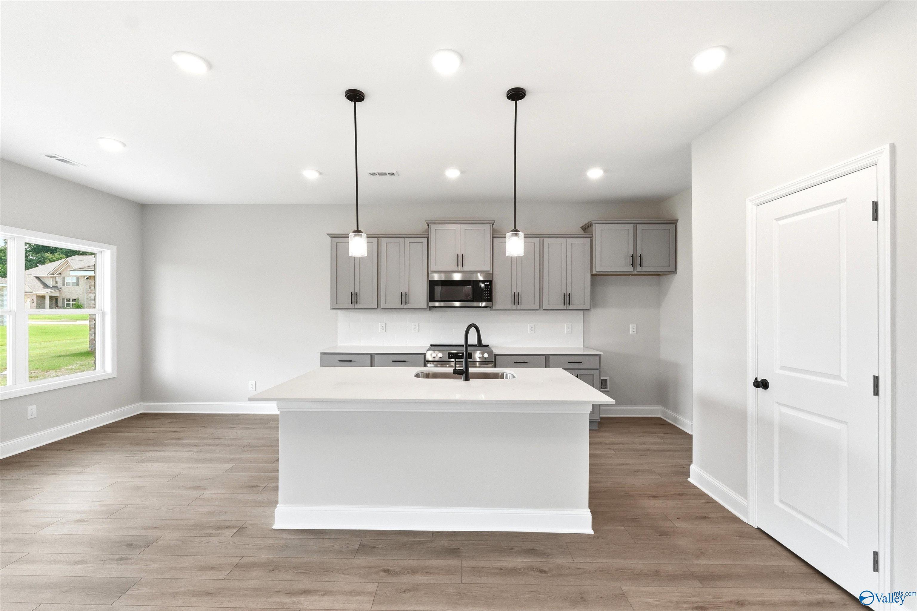 Modern kitchen with gray cabinets, quartz island, and pendant lighting in The Shelby A home at Wood Trail, Toney, Alabama.